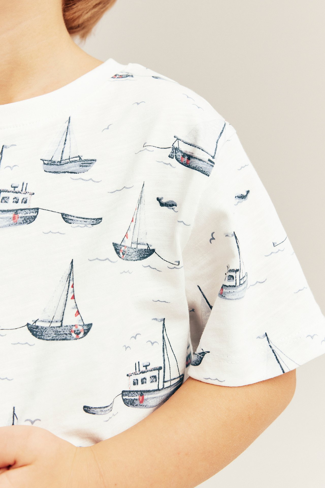 Close-up of a kid wearing an off-white slub jersey t-shirt with an all-over sailboat pattern.