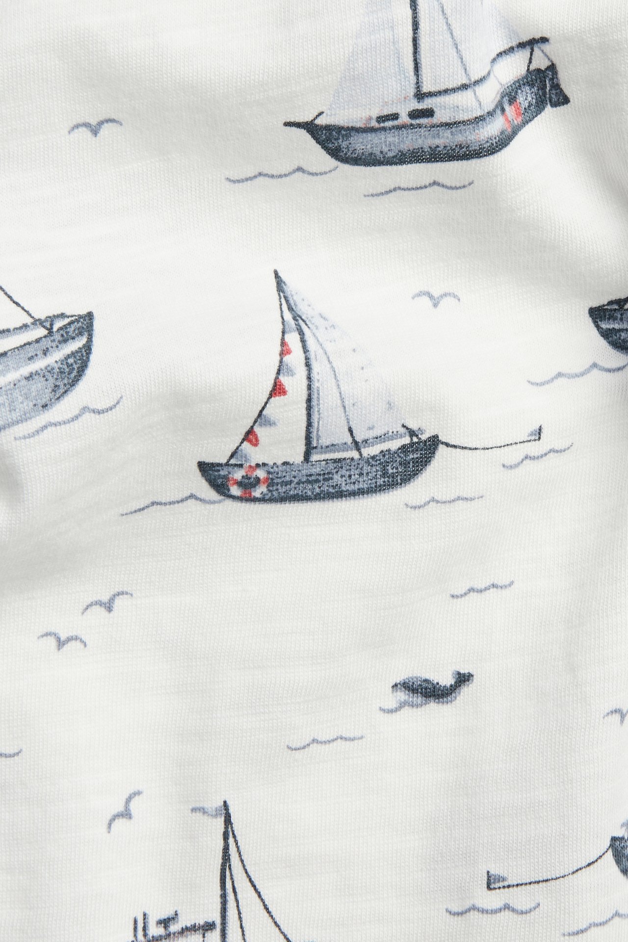 Close-up: off-white slub jersey T-shirt with an all-over sailboat pattern.
