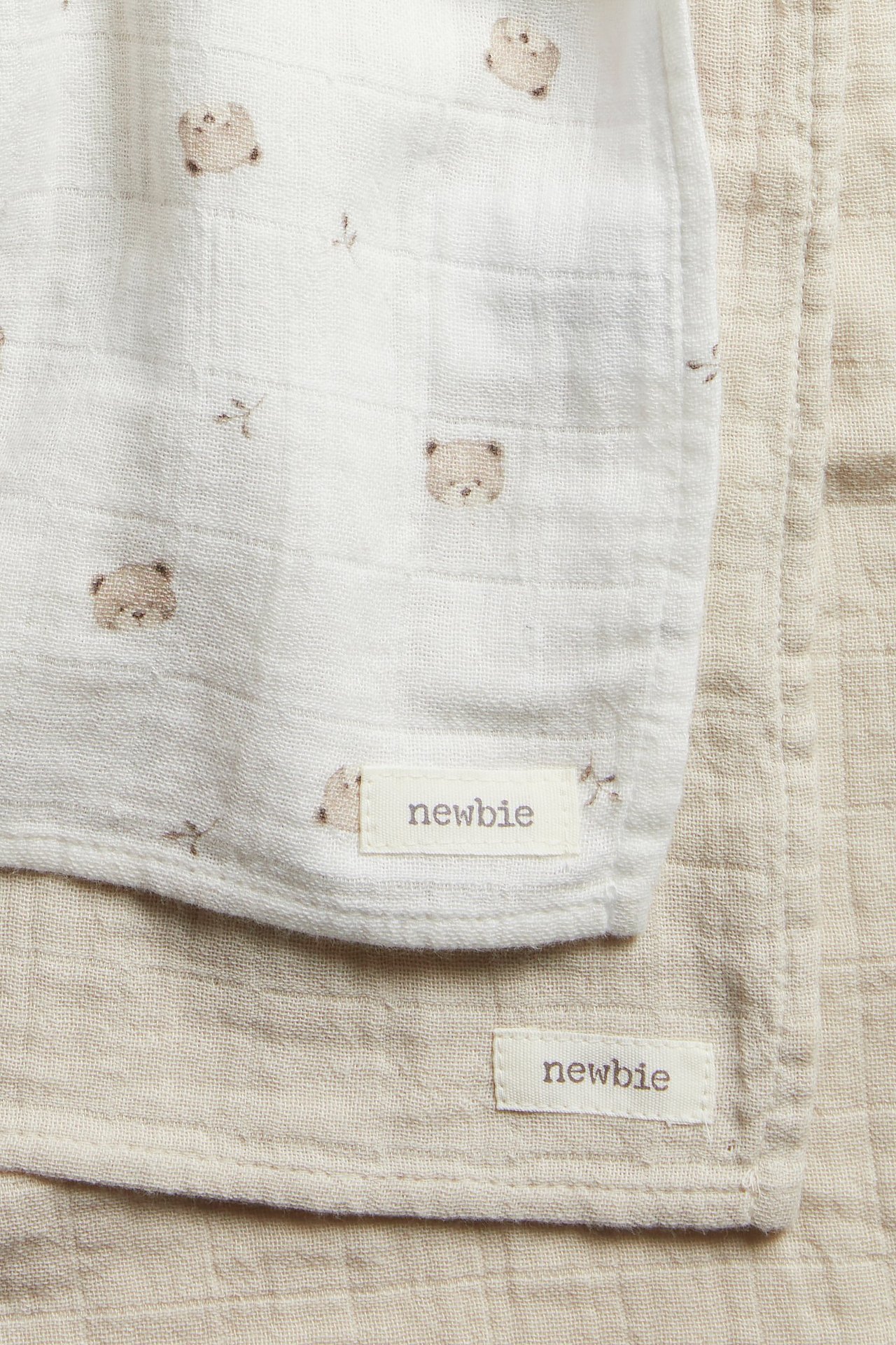 Nahaufnahme von zwei Baumwoll-Musselin-Decken: eine cremefarbene mit Bärenmuster, eine einfarbige hellbeige.