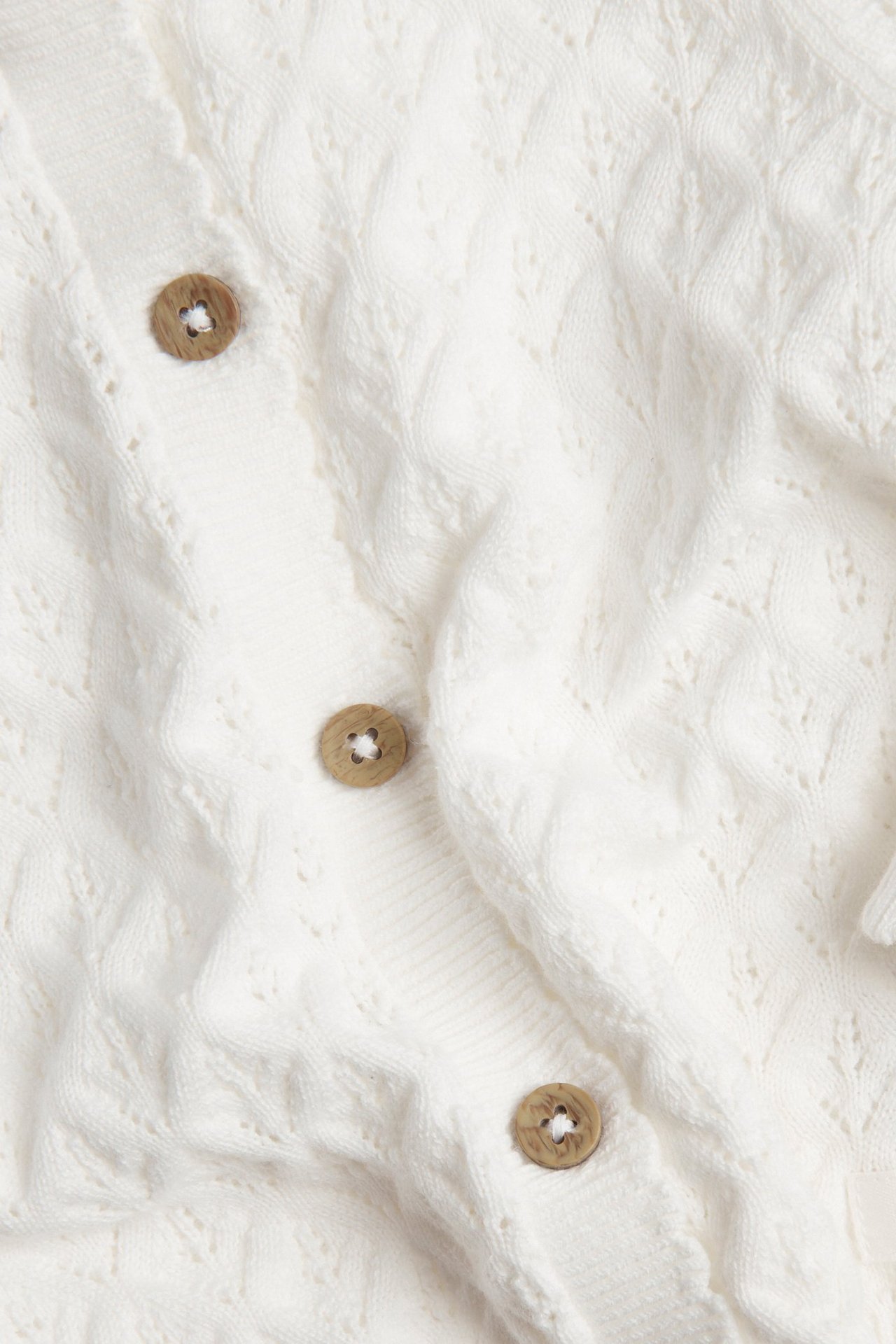 Close-up of an off-white patterned knitted cotton cardigan with light brown wooden buttons.