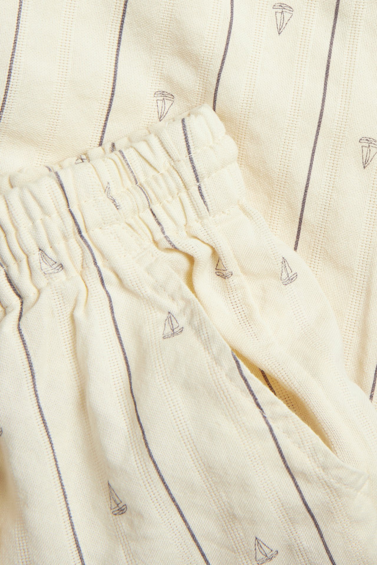 Nahaufnahme cremefarbener Baumwollhosen mit grauen Streifen und Segelboot-Muster, mit elastischem Bund.