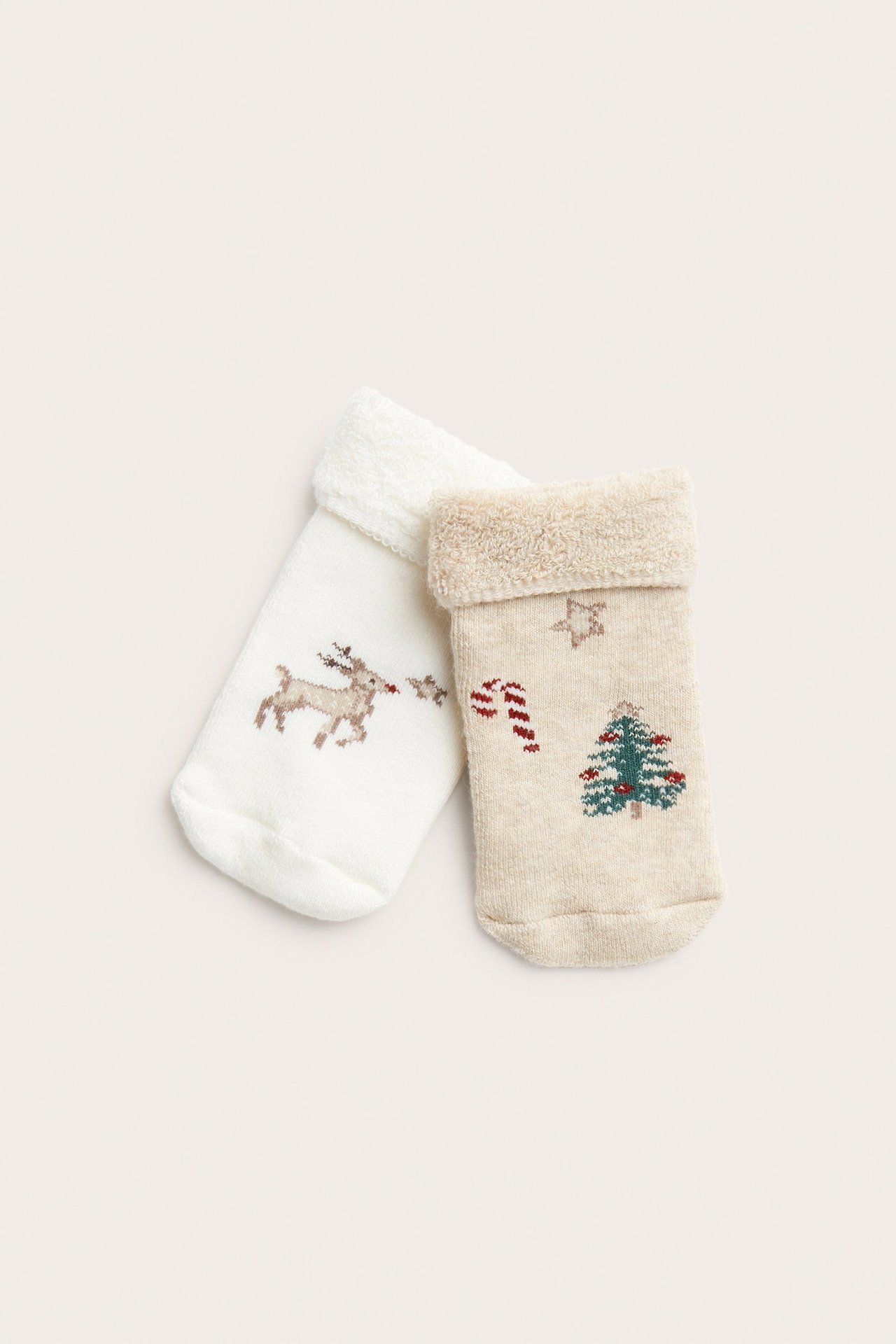 Vorderansicht von zwei Frotteesocken: eine cremeweiß mit Rentier, eine beige mit Weihnachtsbaum.