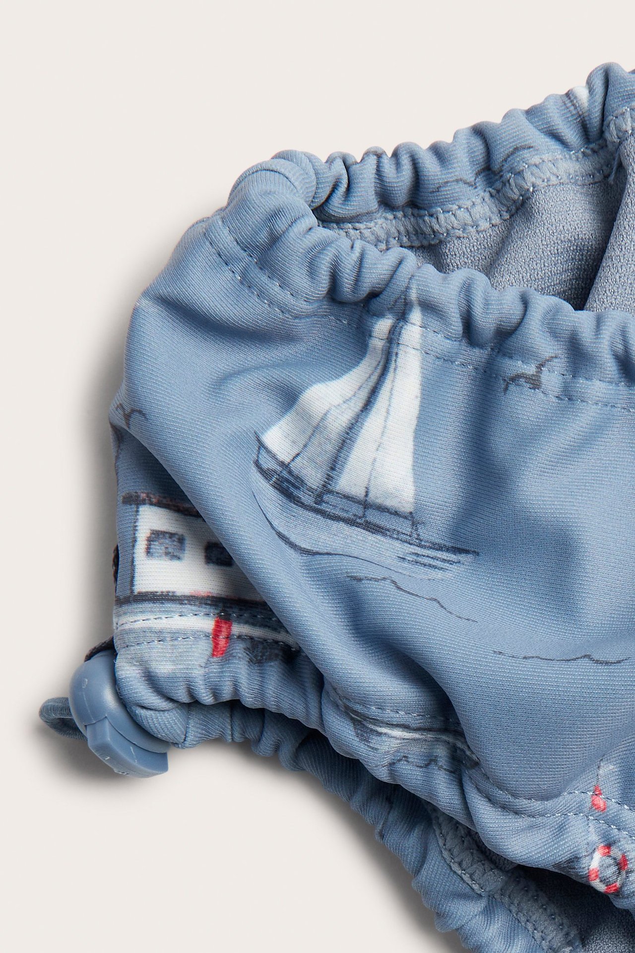 Close-up of blue baby swim briefs with a boat pattern, elasticated edges, and adjustable stoppers.