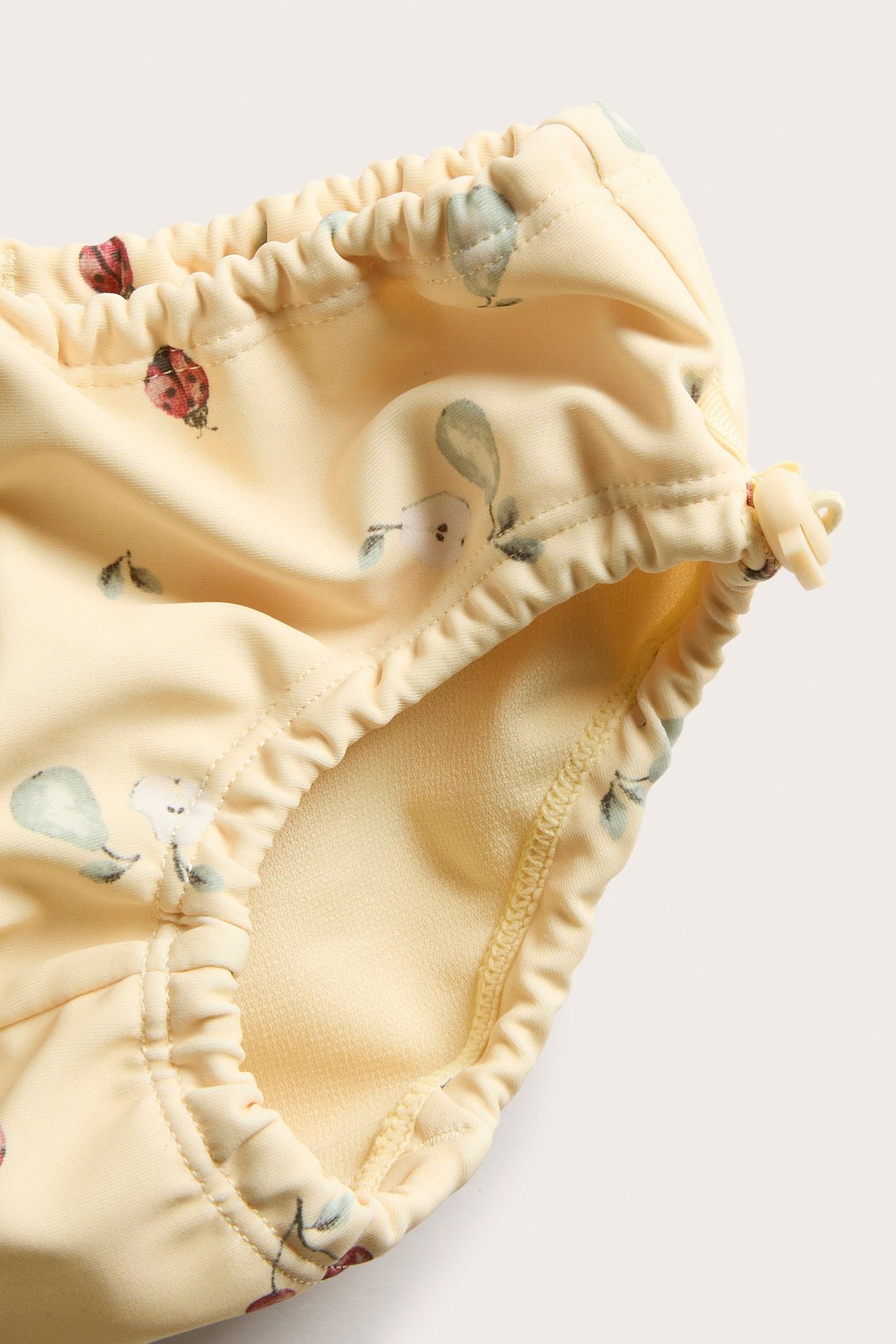 Close-up of yellow baby swim briefs with fruit and ladybug pattern, elasticated waist and legs with stopper.
