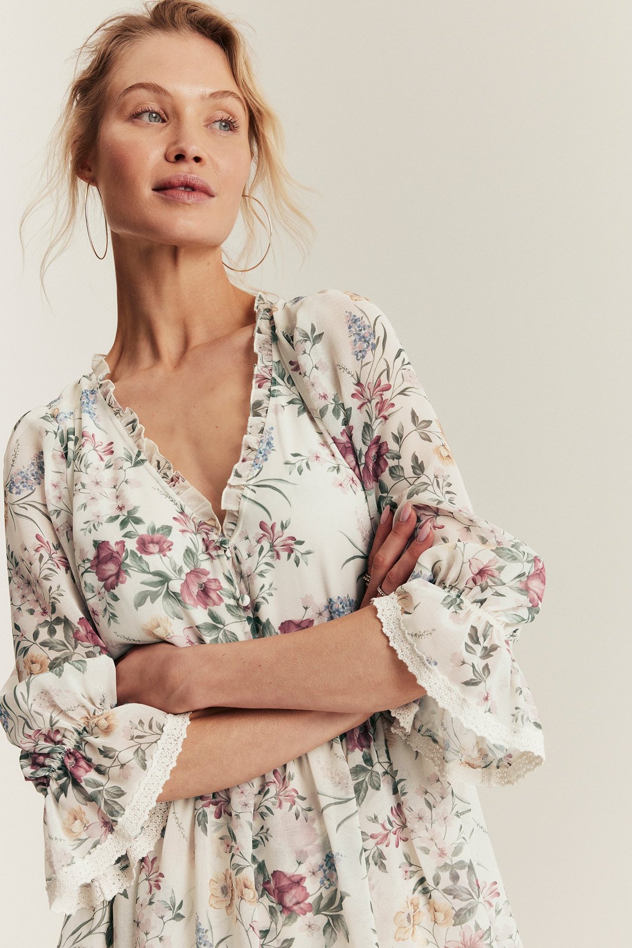 Frau in offweißem, geblümtem Chiffonkleid mit Rüschen, Knöpfen, Halbärrmeln und Creolen, Vorderansicht.