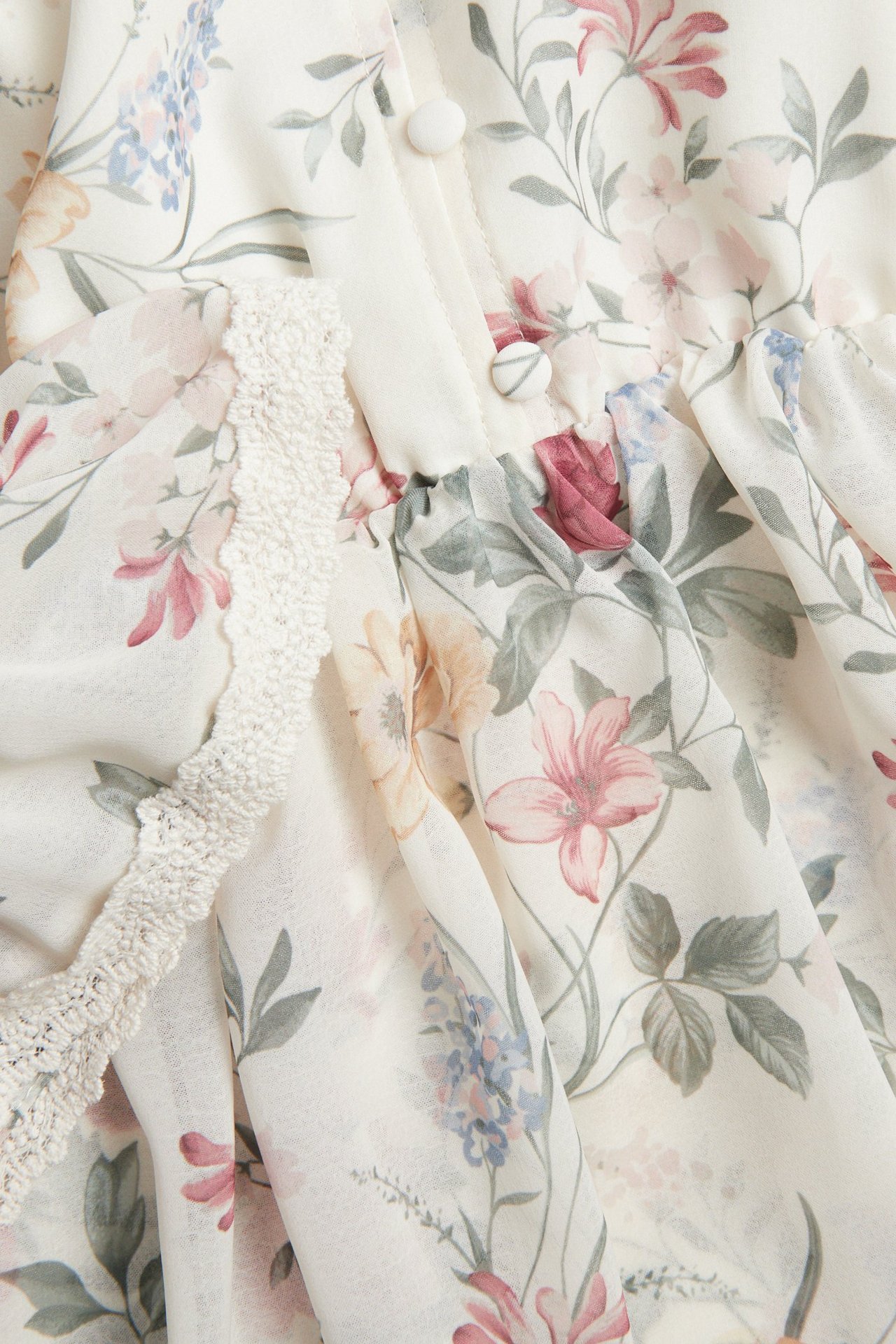 Nahaufnahme eines cremeweißen geblümten Chiffonkleides mit rosa, blauen, grünen Blumen und stoffbezogenen Knöpfen.
