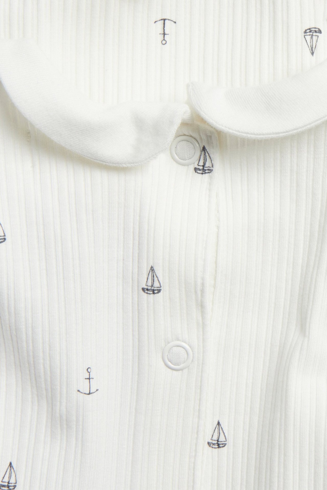 Close-up: Off-white ribbed baby bodysuit with collar, dark blue sailboat and anchor pattern, and snap buttons.