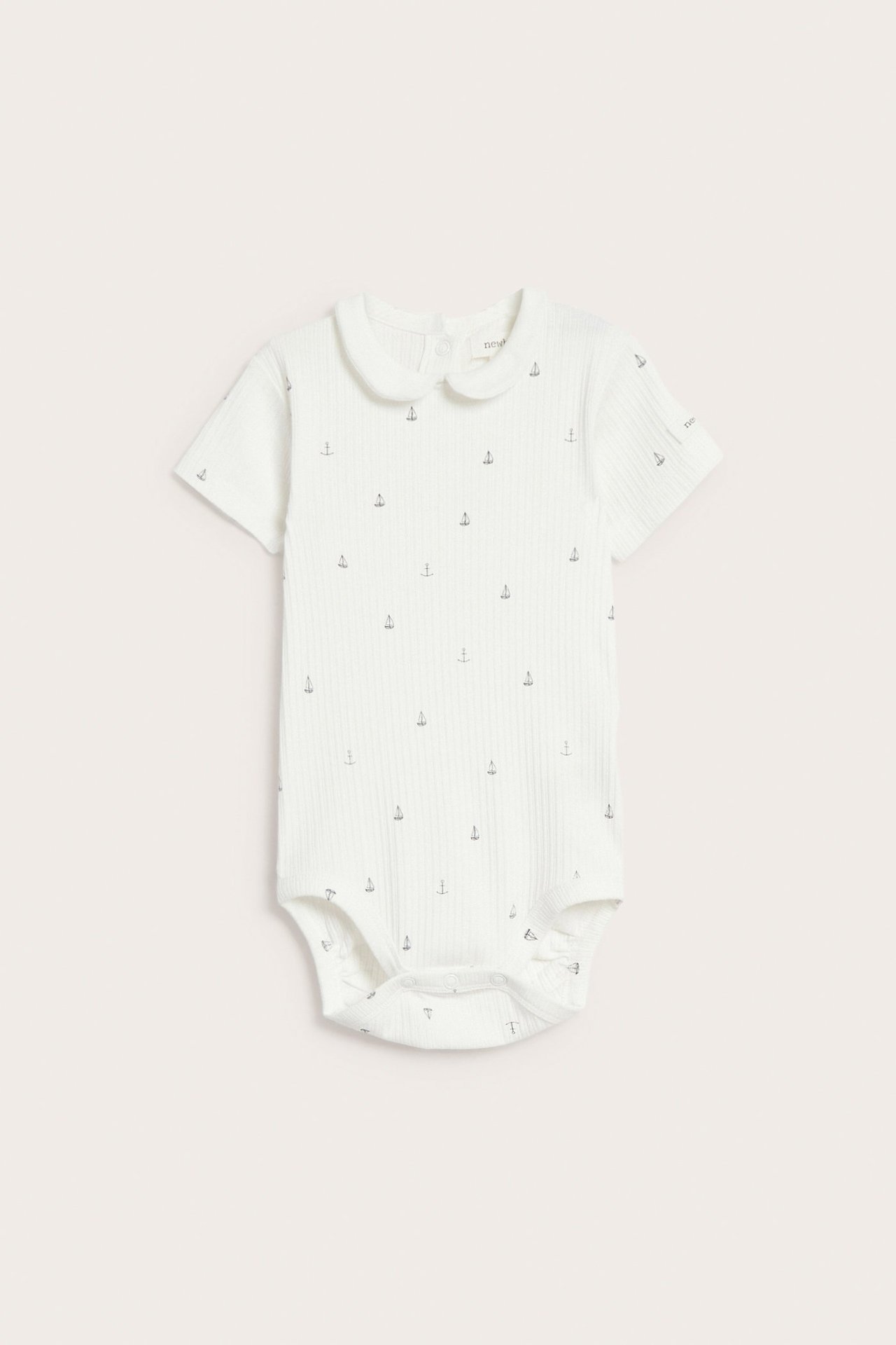 Front view of an offwhite ribbed baby bodysuit with short sleeves, a collar, and small anchor patterns.