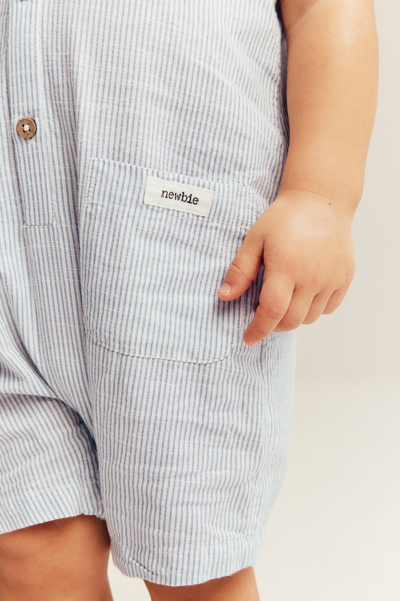 Close-up of a baby's light blue striped cotton romper, with a wooden button and patch pocket.