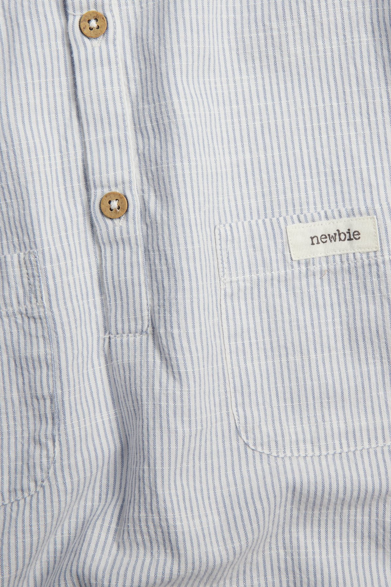 Nahaufnahme eines Baby-Rompers aus blau-weiß gestreifter Baumwolle mit Holzknöpfen und aufgesetzter Tasche.