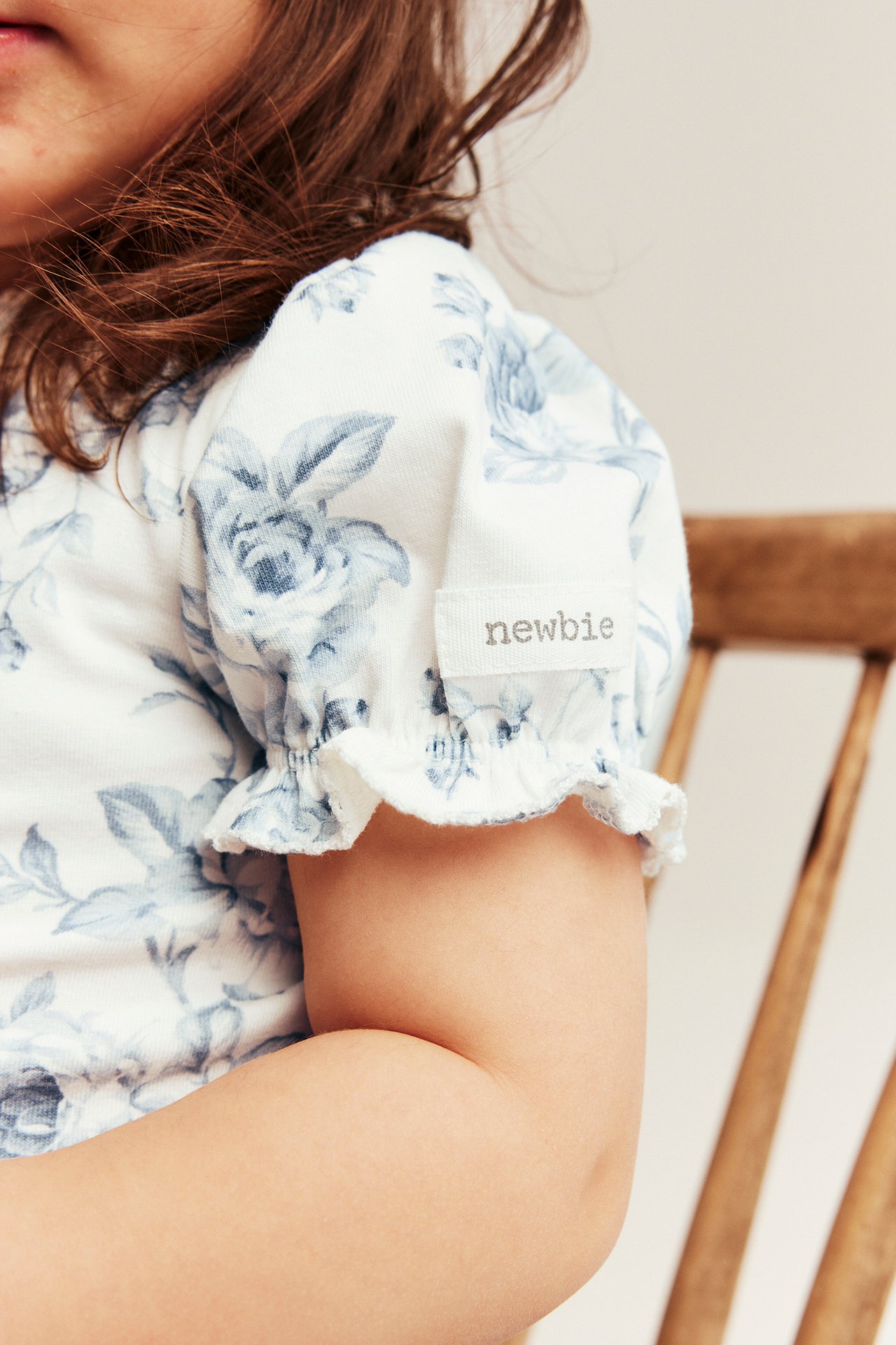 Close-up of a kid wearing an off-white floral short-sleeved bodysuit with blue flowers and ruffled puff sleeves.