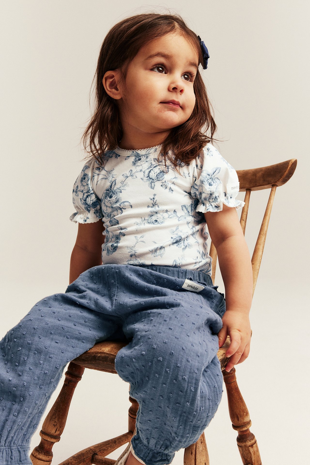 Front view of a kid wearing an offwhite floral short-sleeved bodysuit and blue textured pants.