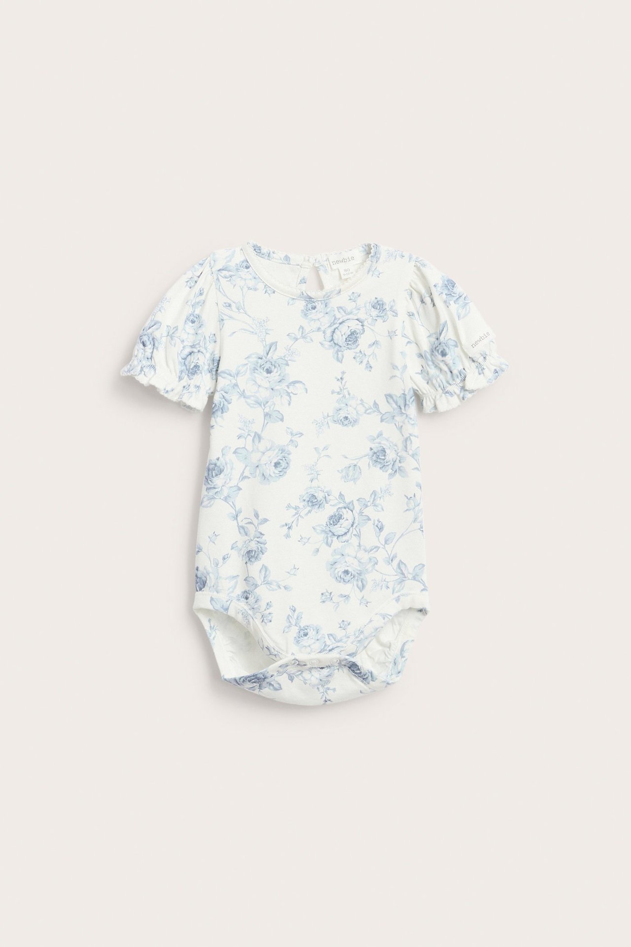 Vorderansicht: Cremefarbener Baby-Body, blaues Blumenmuster, kurze Puffärmel, Gummibündchen und Picot-Rand.
