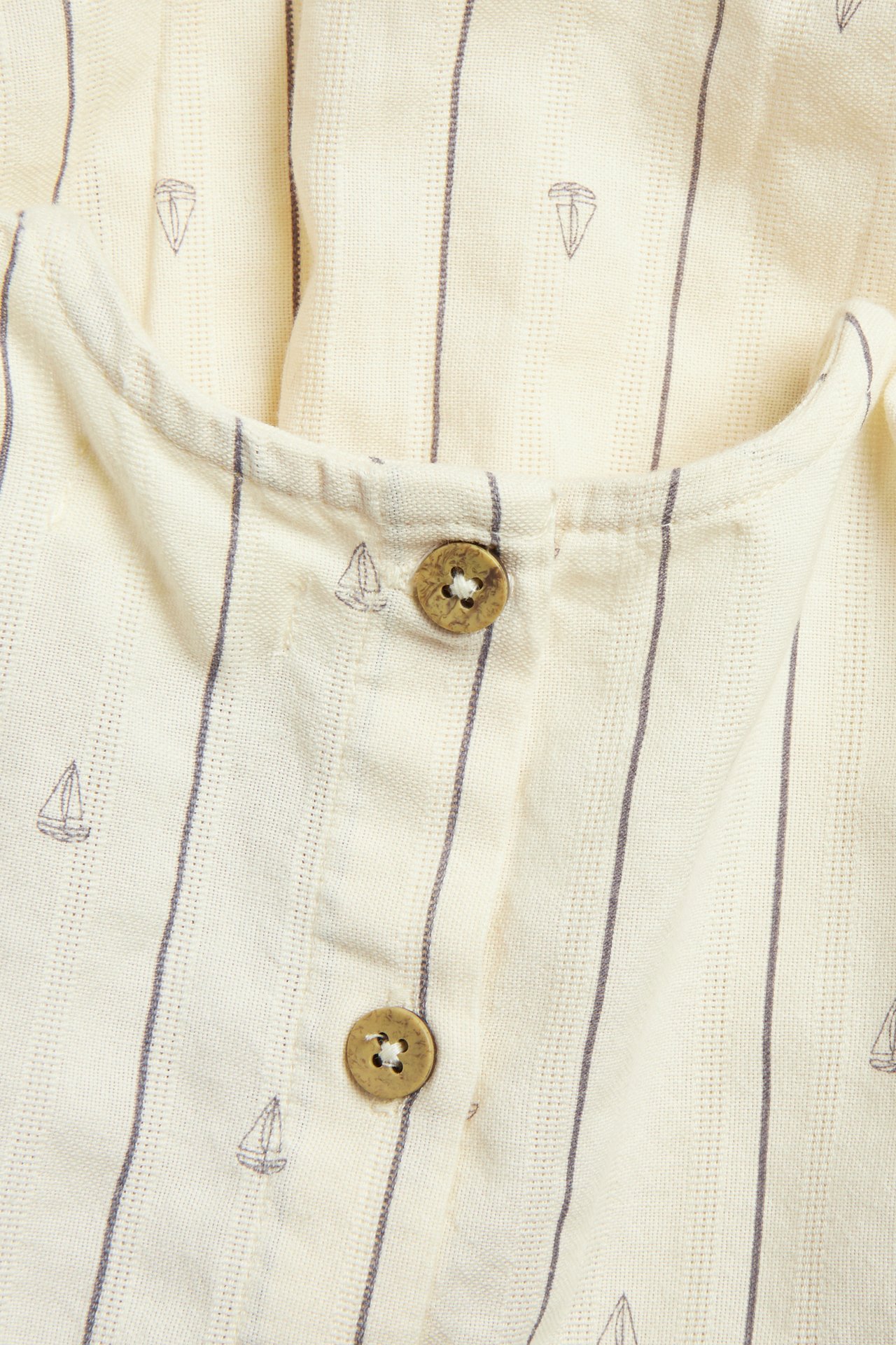 Close-up of a white cotton dress with grey stripes, sailboat prints, and brown buttons.