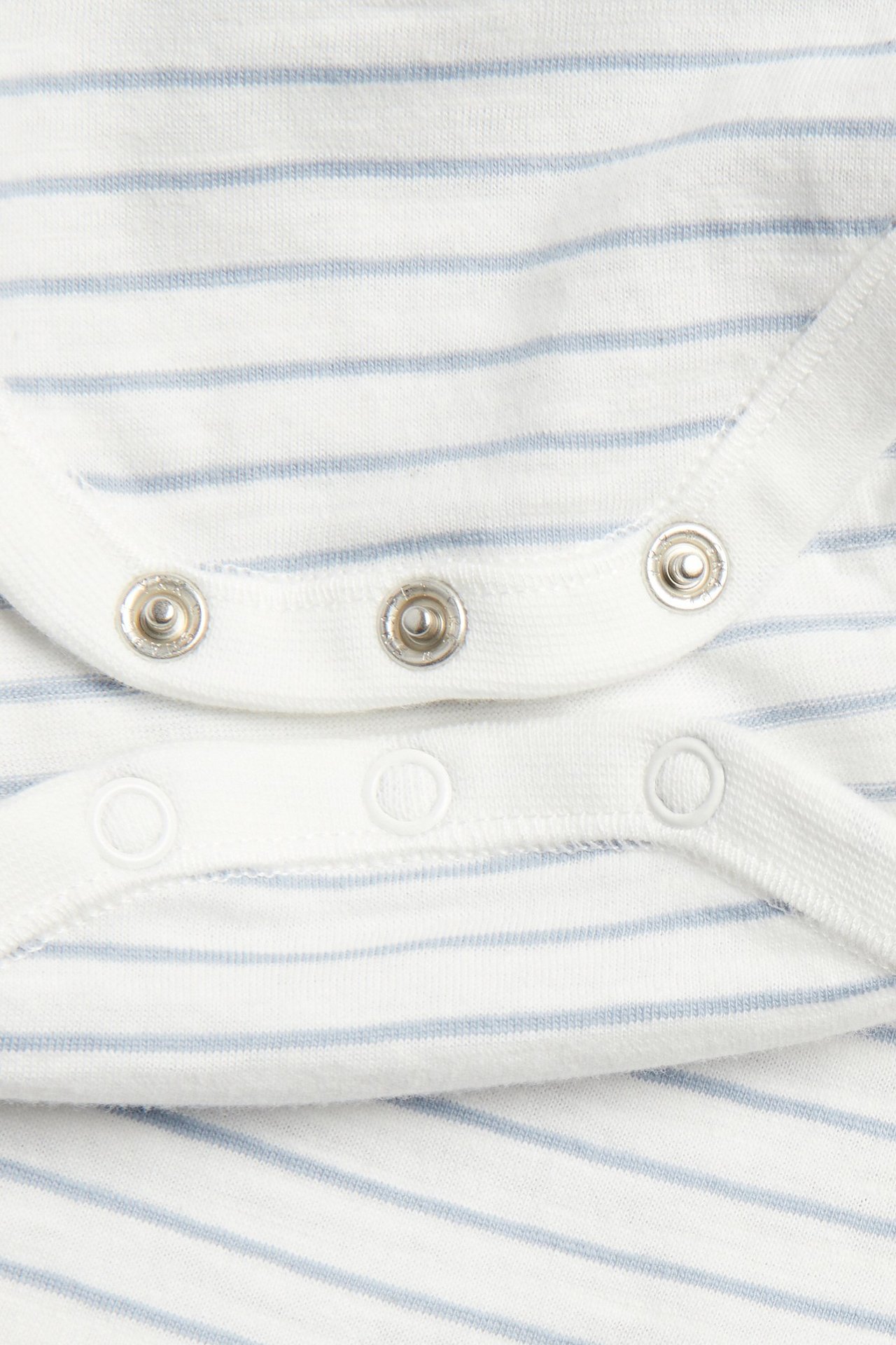 Close-up of snap fasteners on an off-white baby bodysuit with light blue stripes.