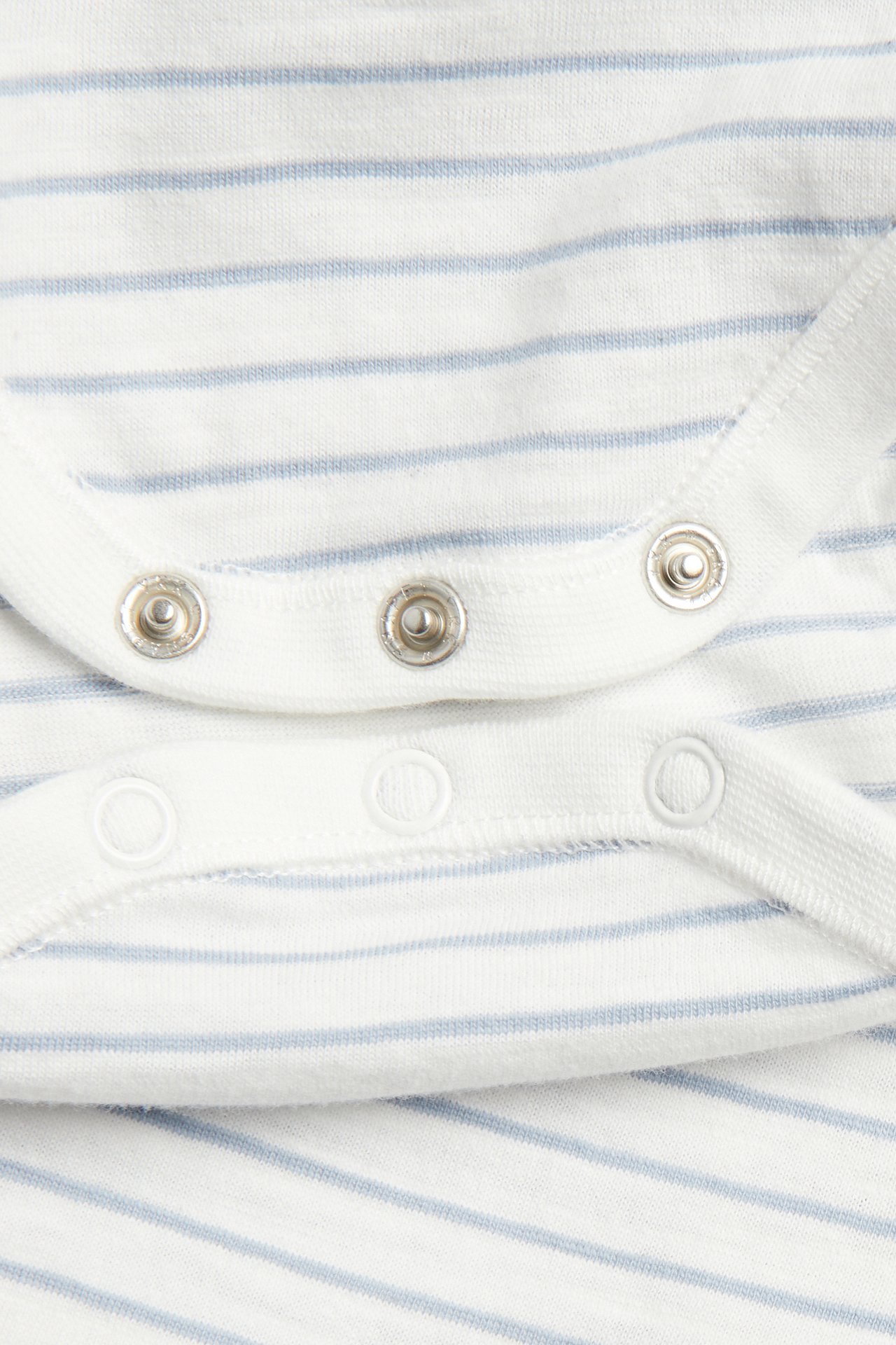 Nahaufnahme von Druckknöpfen eines gestreiften off-white Baby-Bodys mit hellblauen Streifen.