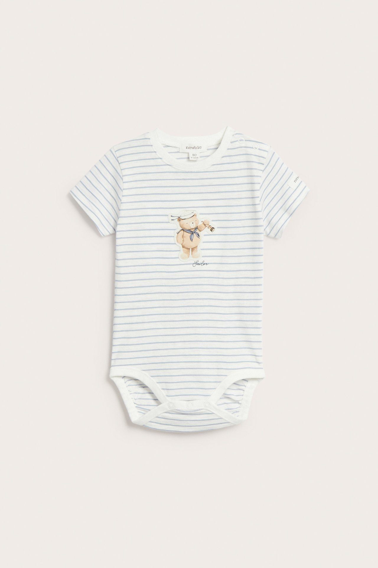 Front view of a baby's off-white short-sleeved cotton bodysuit with light blue stripes, featuring a sailor bear appliqué.
