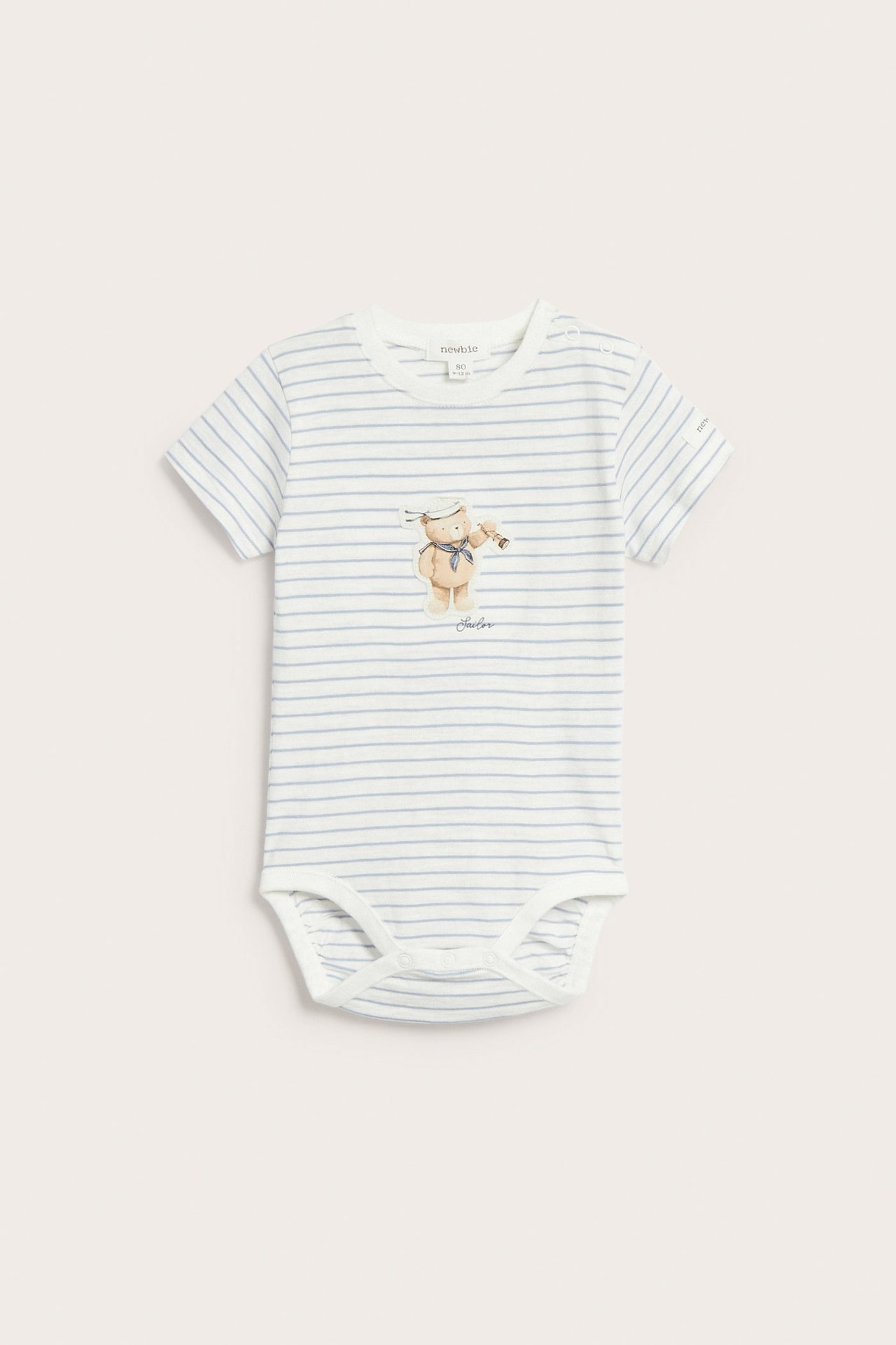 Vorderansicht eines kurzärmeligen Baby-Bodys aus cremefarbener Baumwolle mit hellblauen Streifen und Seemanns-Bären-Applikation.