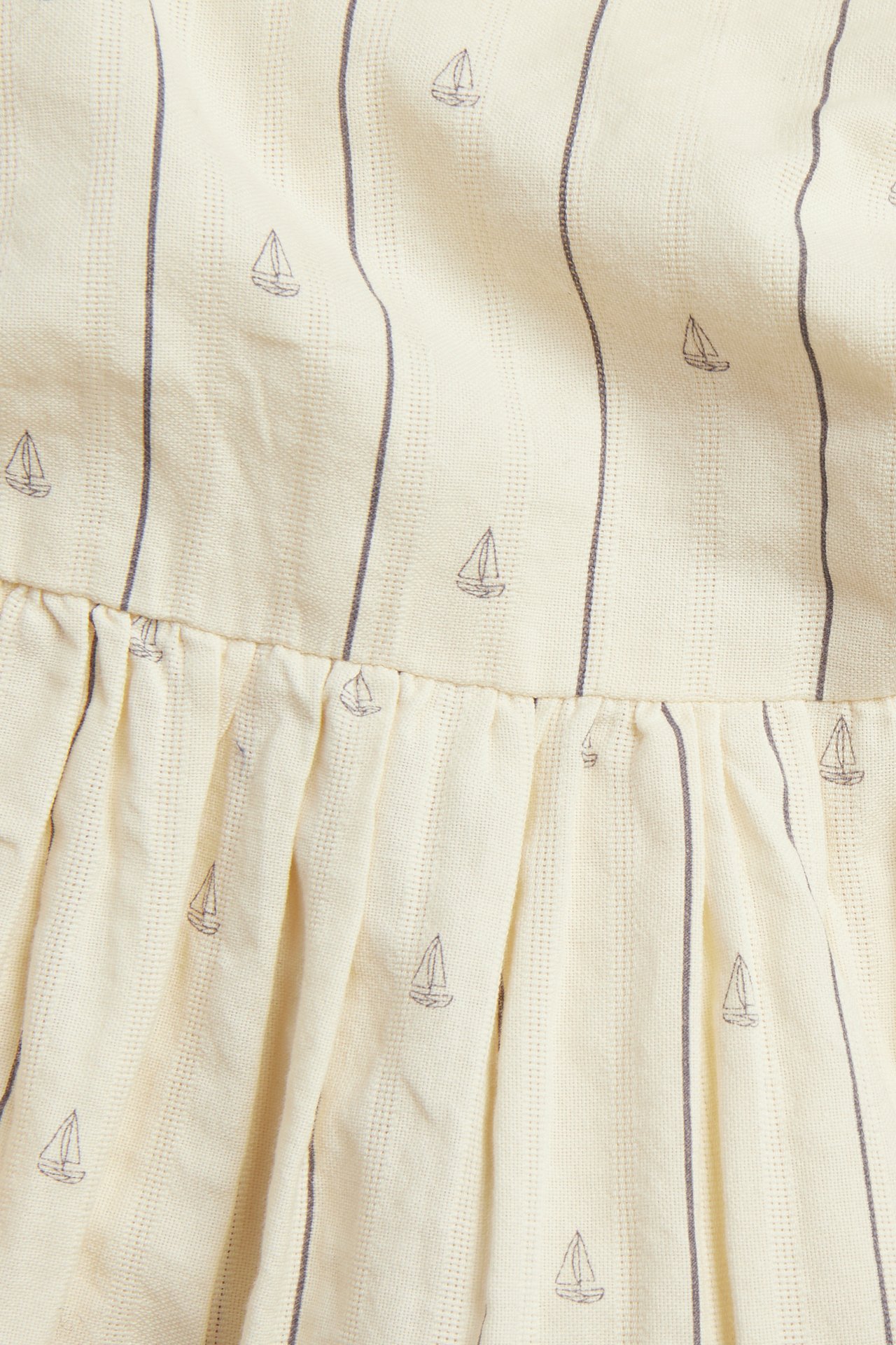 Nahaufnahme von weißem Baumwollkleiderstoff mit dünnen dunklen Streifen und kleinen Segelboot-Prints, zeigt eine geraffte Naht.