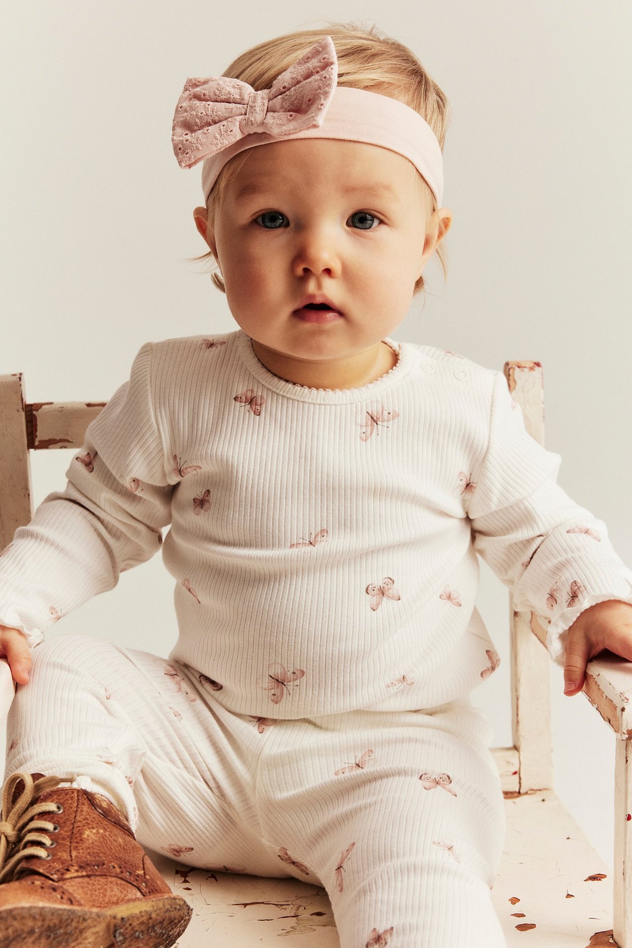 Front view: Kid girl in white striped boat print dress, dark blue bow, and brown sandals.