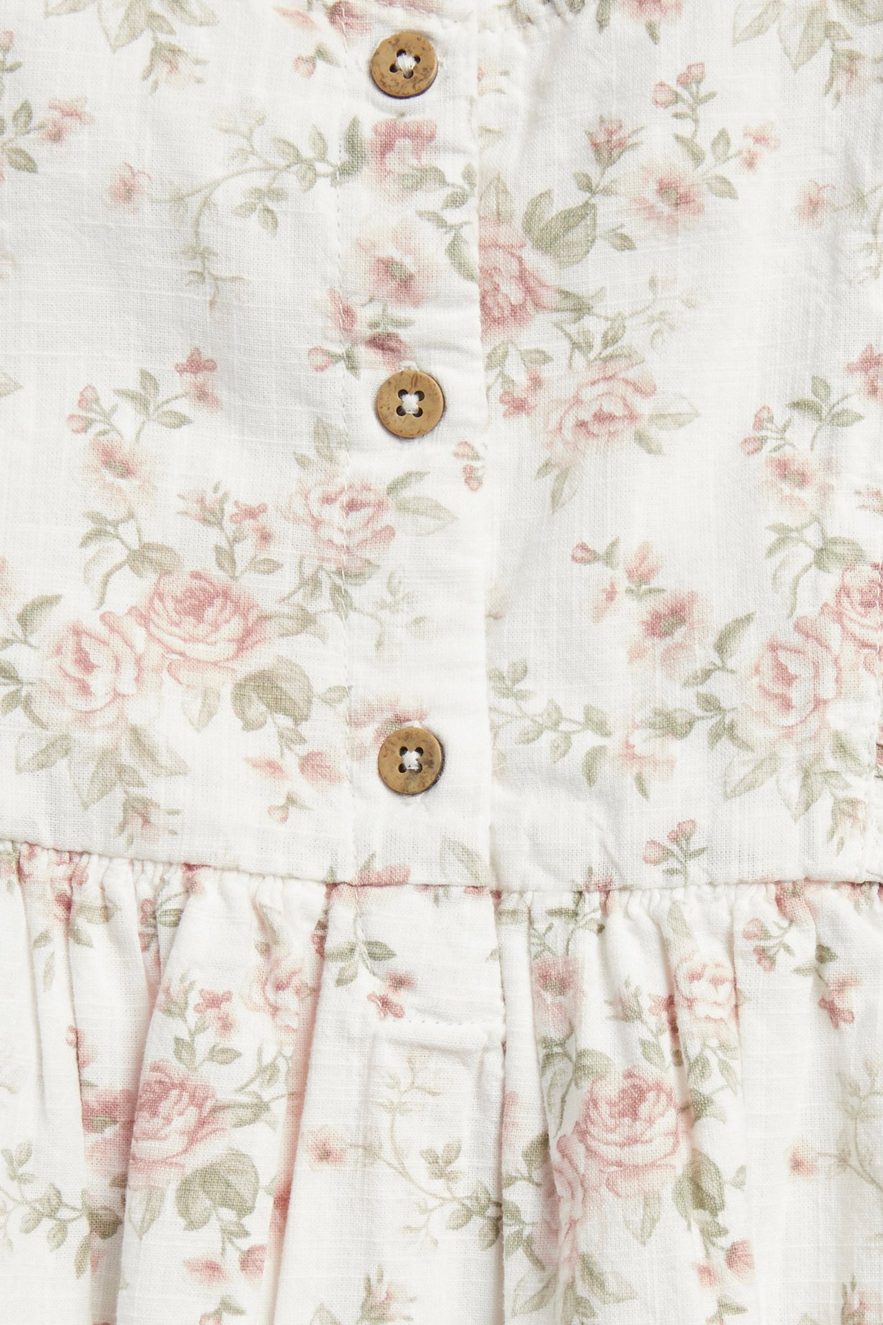 Close-up of an off-white dress with a floral pattern of pink roses, green leaves, and wooden buttons.
