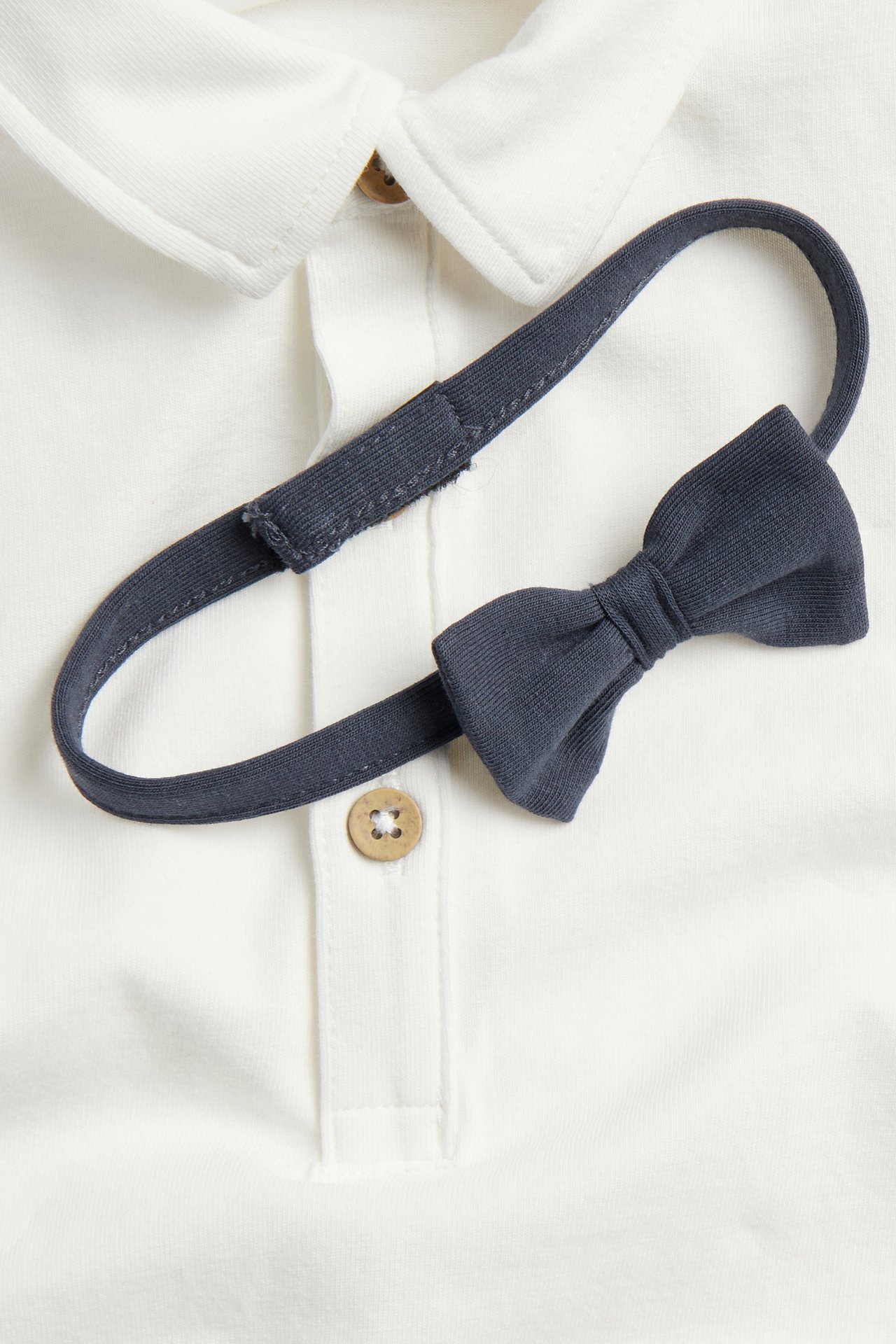 Close-up of an off-white cotton short-sleeved bodysuit with a collar and a dark grey detachable bow tie.