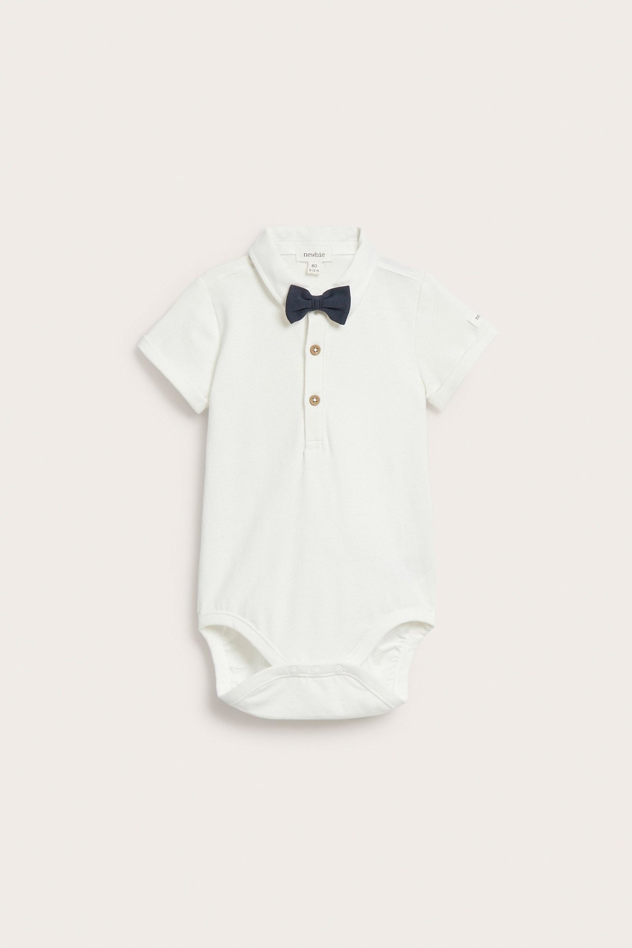 Front view of an off-white baby short-sleeved bodysuit with collar, dark blue detachable bow tie, and snap fasteners.