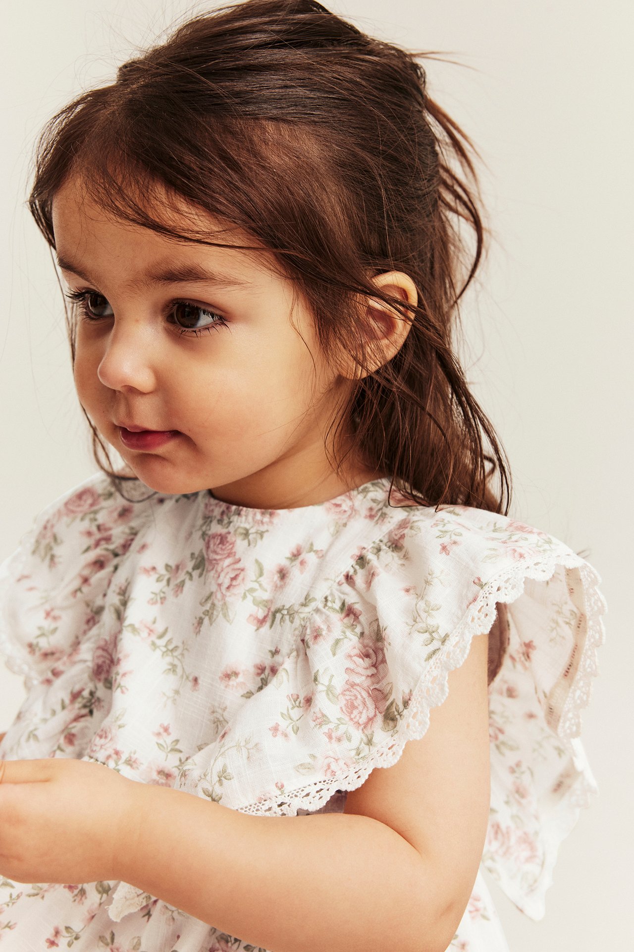 Nahaufnahme, Seitenansicht eines Kindes in einem cremeweißen Blumenkleid mit Rüschenärmeln und Spitzenborte.