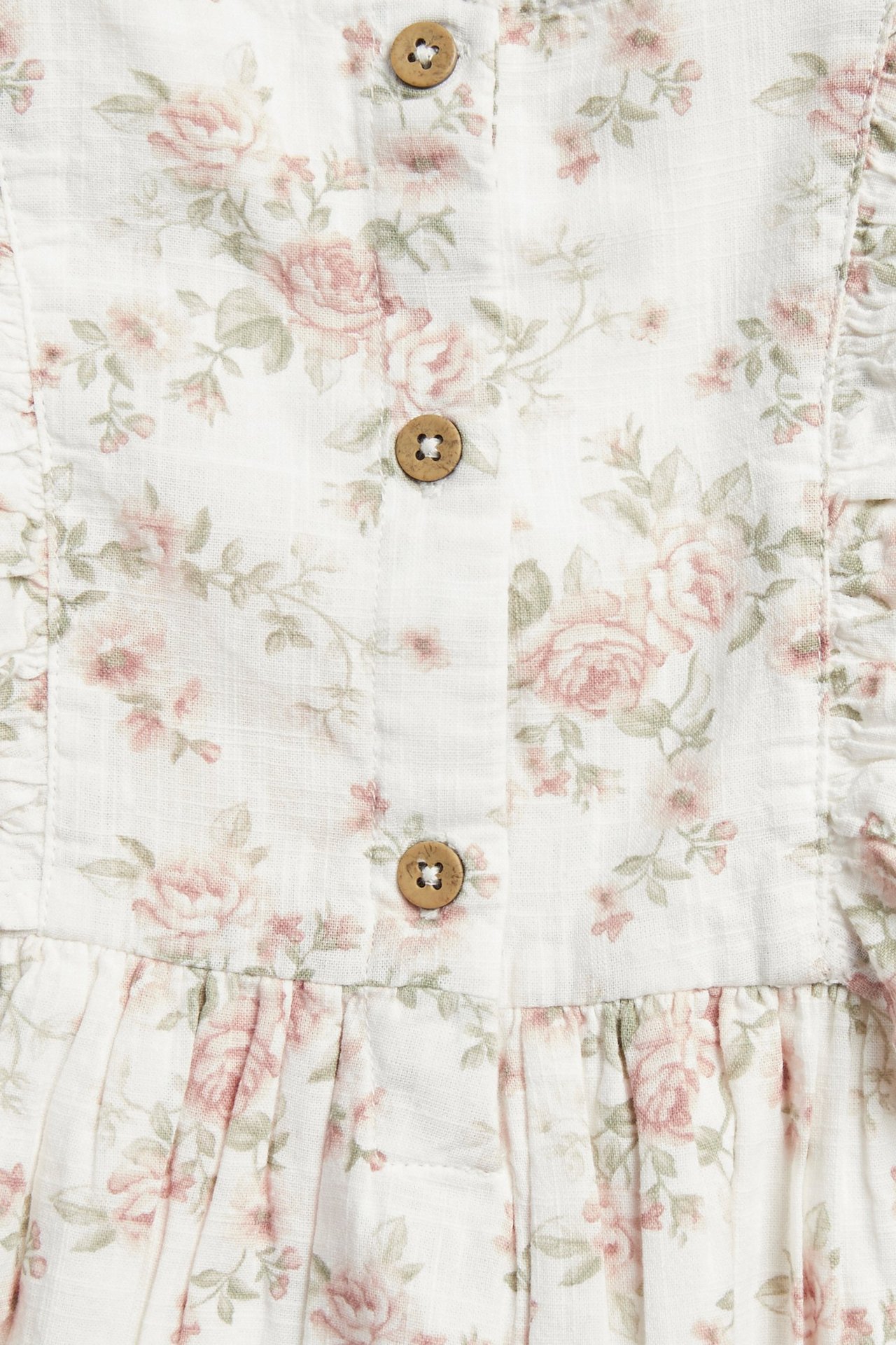Close-up of an off-white floral dress with pink roses, ruffles, and wooden back buttons.