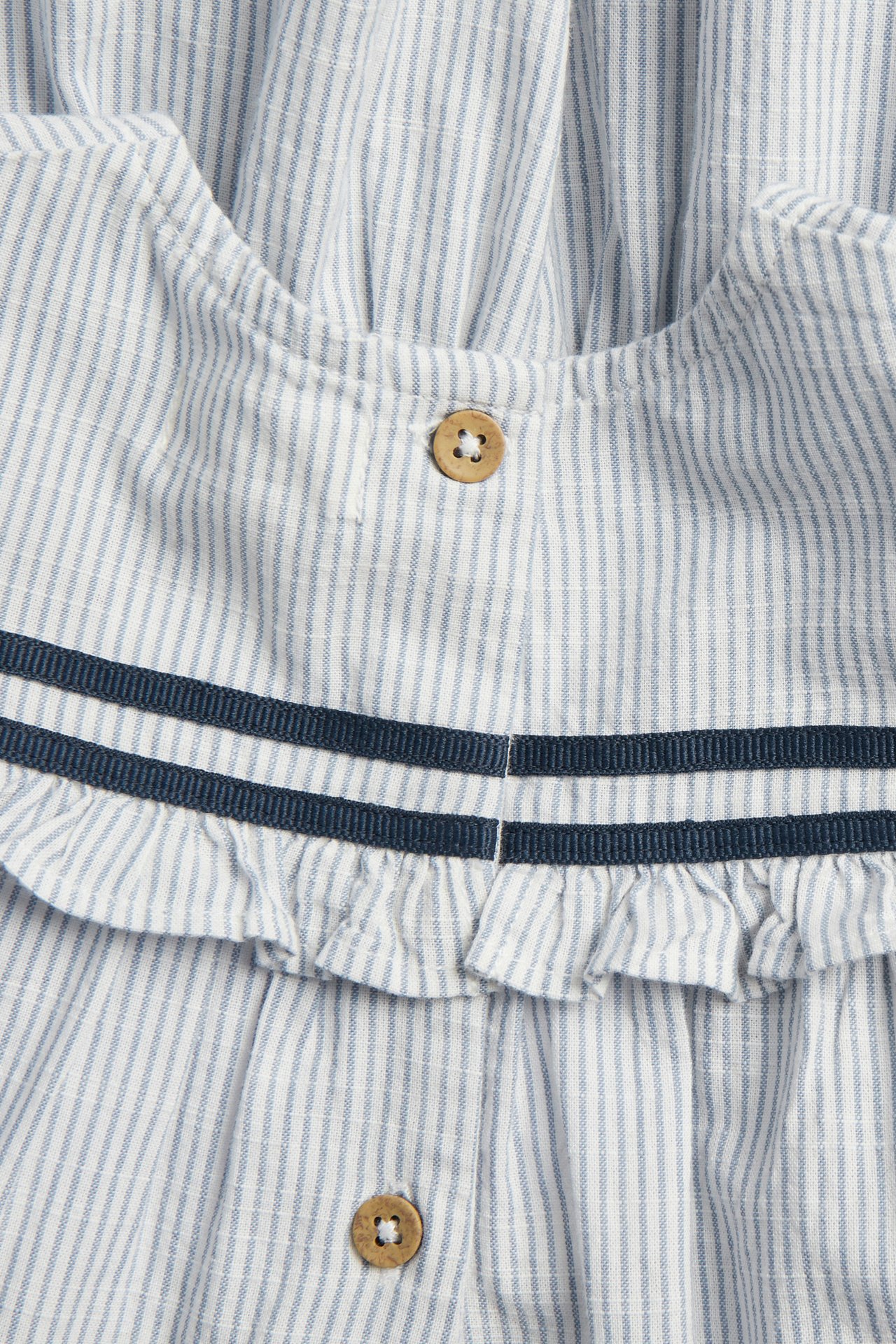 Close-up of a kid's blue and white striped cotton dress with a ruffled yoke, two navy ribbons, and wooden buttons.