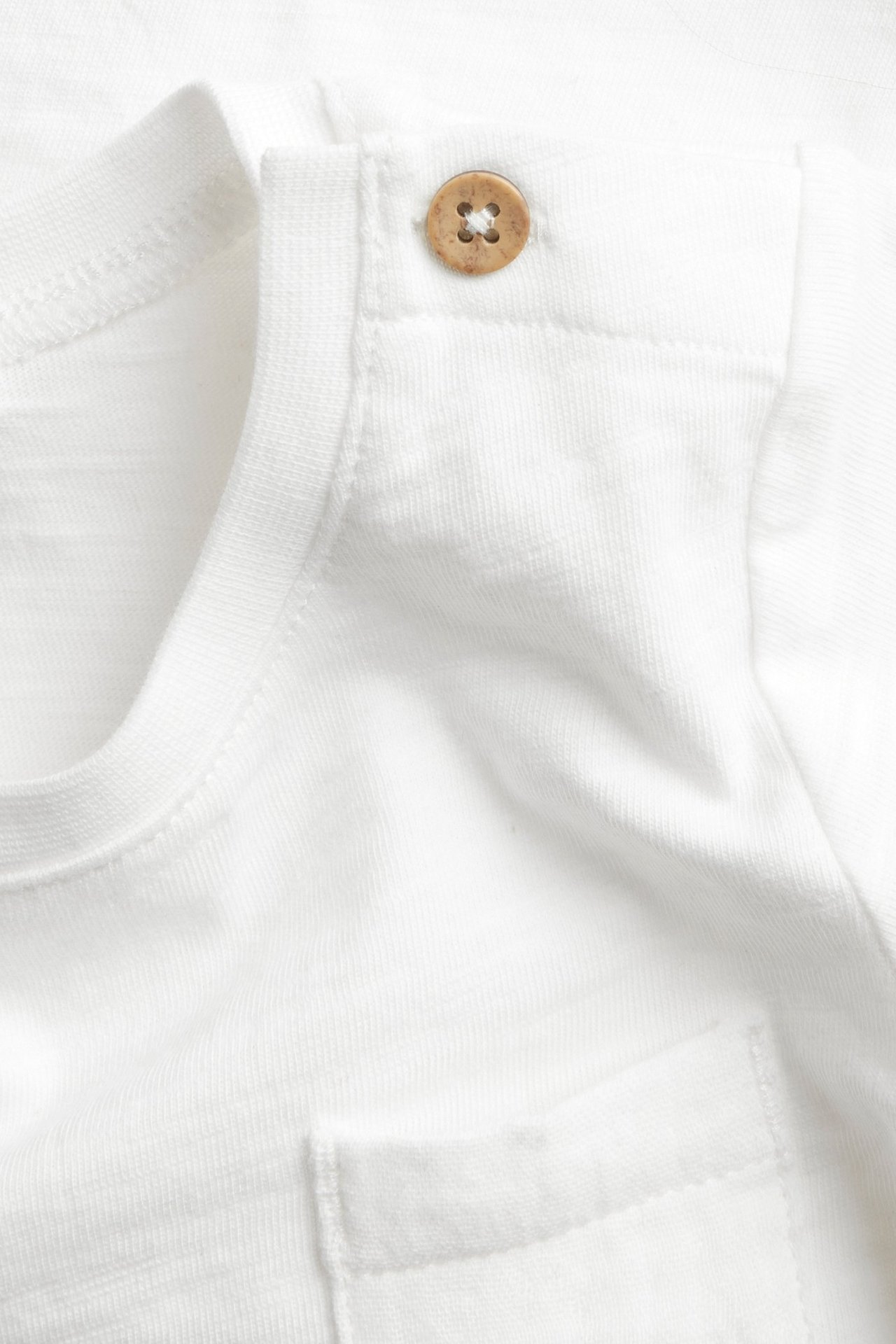 Close-up: Off-white cotton slub jersey baby bodysuit, wooden shoulder button, chest pocket.