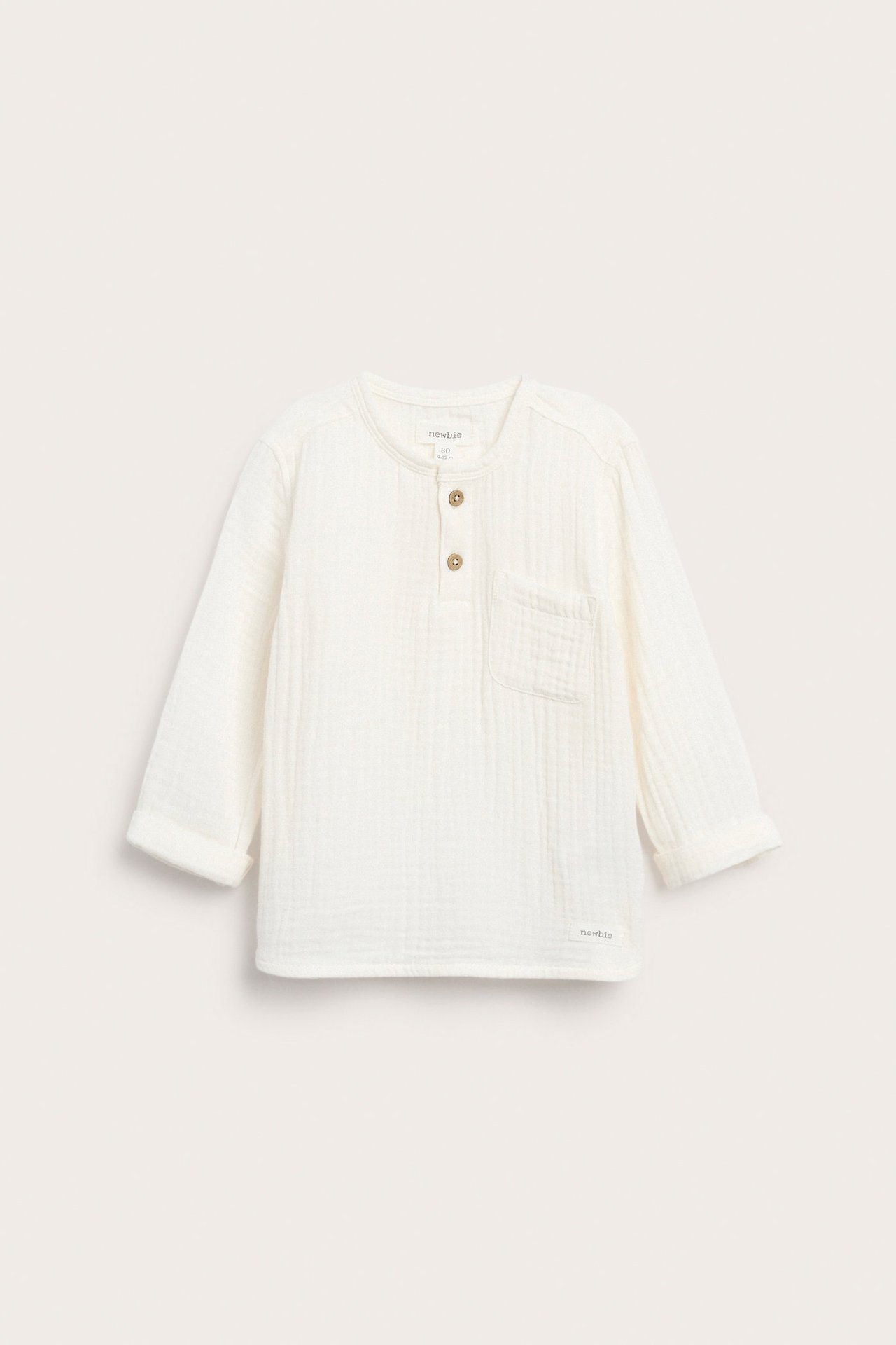 Front view of an off-white baby long-sleeved muslin top with front buttons, a chest pocket, and rolled-up sleeves.