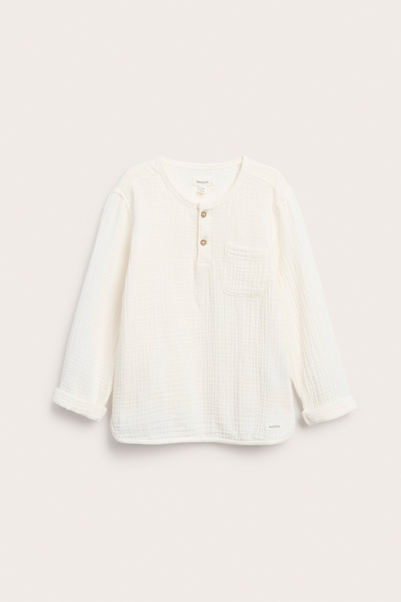 Vorderansicht eines cremefarbenen Langarmshirts aus Baumwollmusselin mit Knopfleiste, Brusttasche und hochgekrempelten Ärmeln.