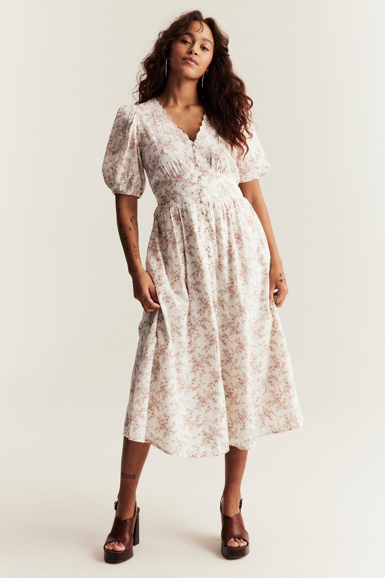 Front view of a woman in an off-white floral cotton midi dress, puff sleeves, and brown platform sandals.