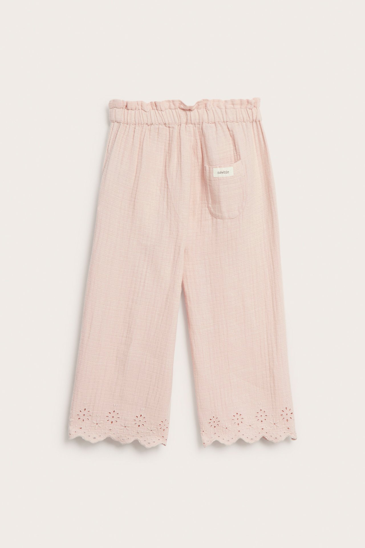 Front view of light pink woven cotton pants with embroidered scalloped hems, elastic waist, and pockets.