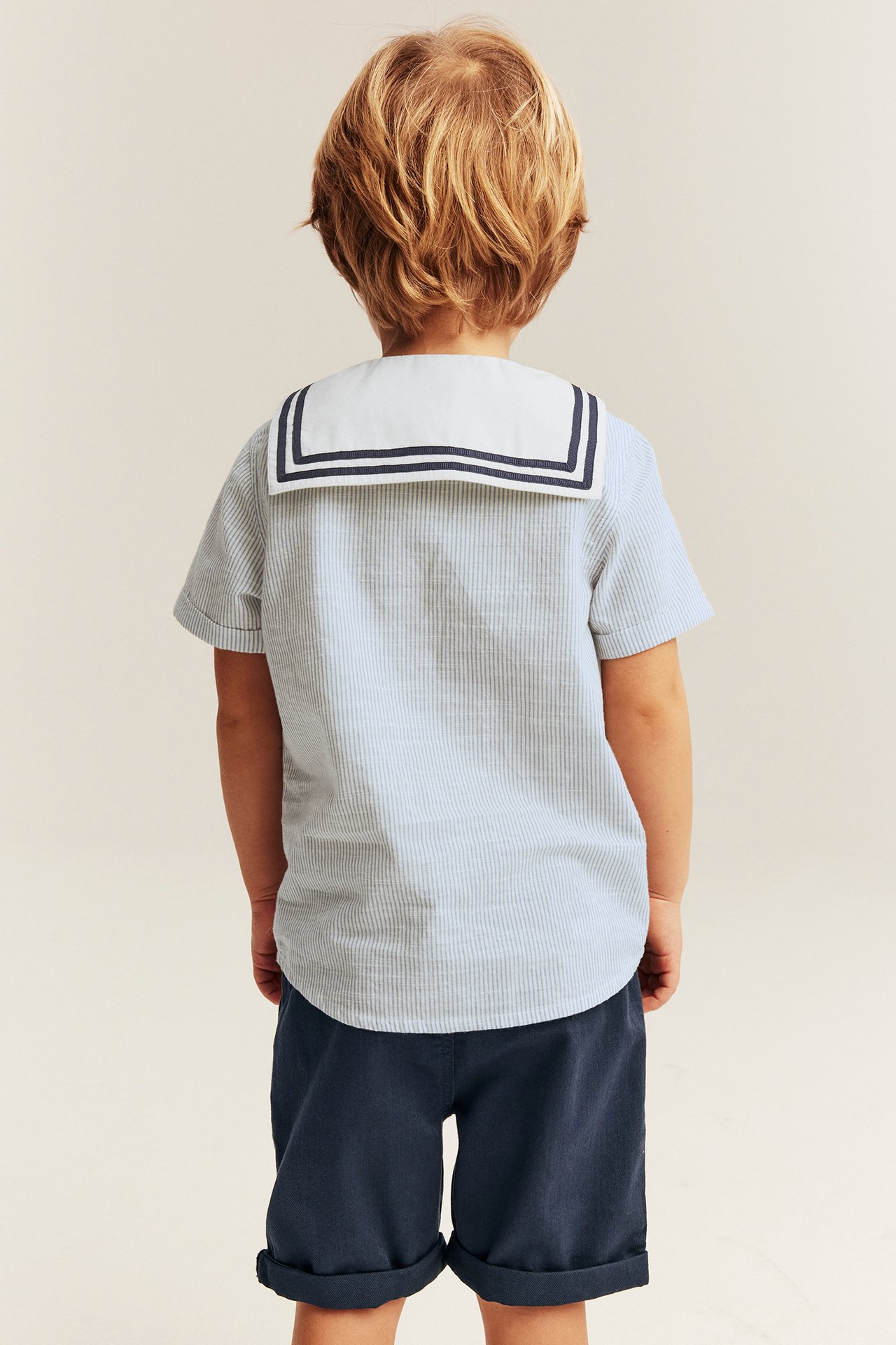 Kinder-Rückenansicht, hellblau gestreiftes Baumwollhemd mit weißem Matrosenkragen und dunkelblauen Shorts.