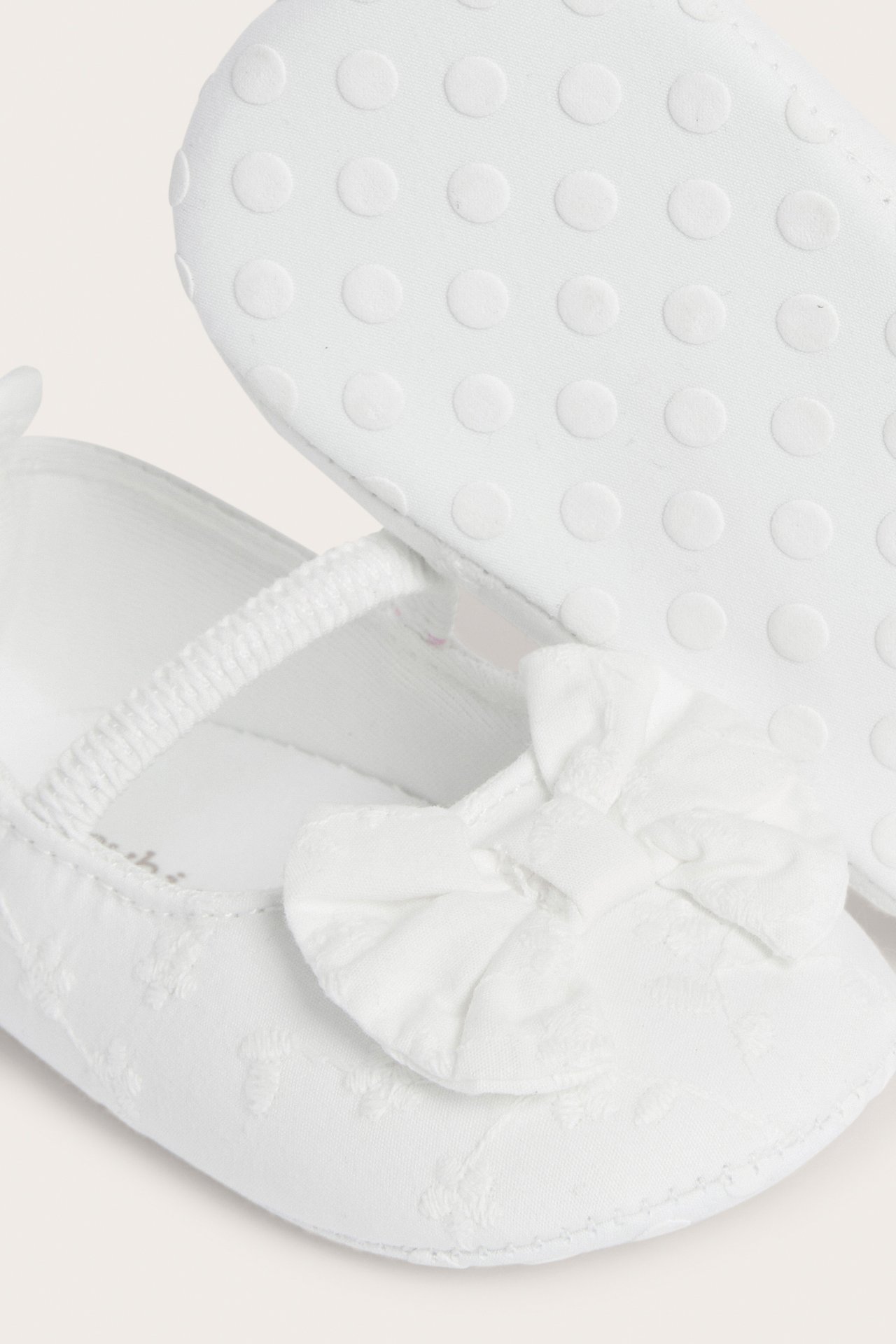 Close-up of off-white embroidered woven cotton baby ballerina shoes with elastic strap, front bow, and anti-slip soles.