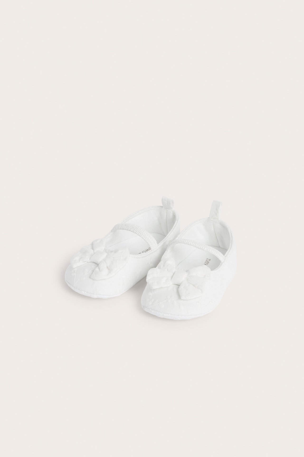 Front view of off-white embroidered cotton baby ballet shoes with elastic strap and front bow.