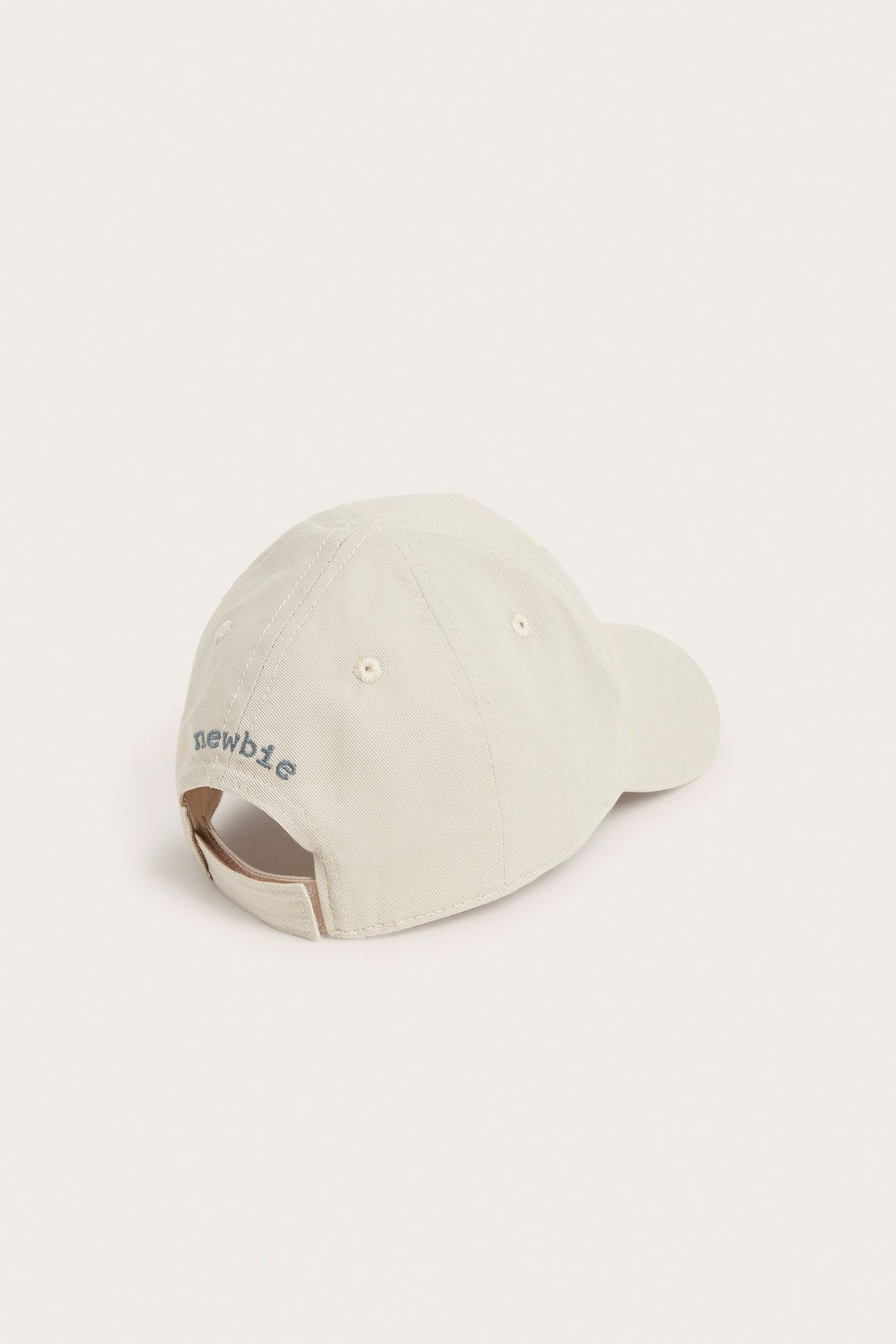 Rear-side view of a beige cotton cap with embroidered "newbie" text and an adjustable back strap.