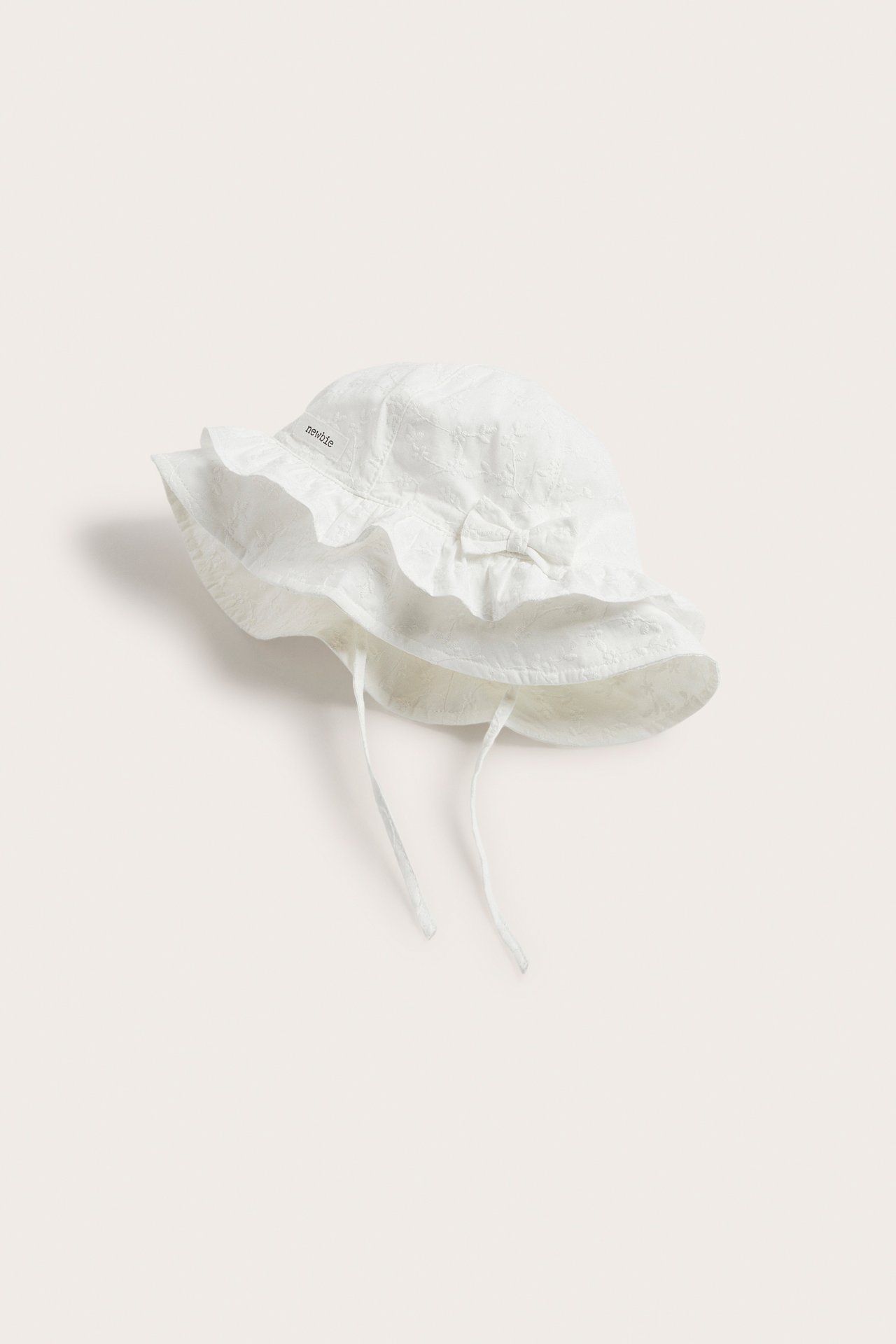 Off-white baby sun hat with floral embroidery, ruffled brim, front bow, and tie straps.