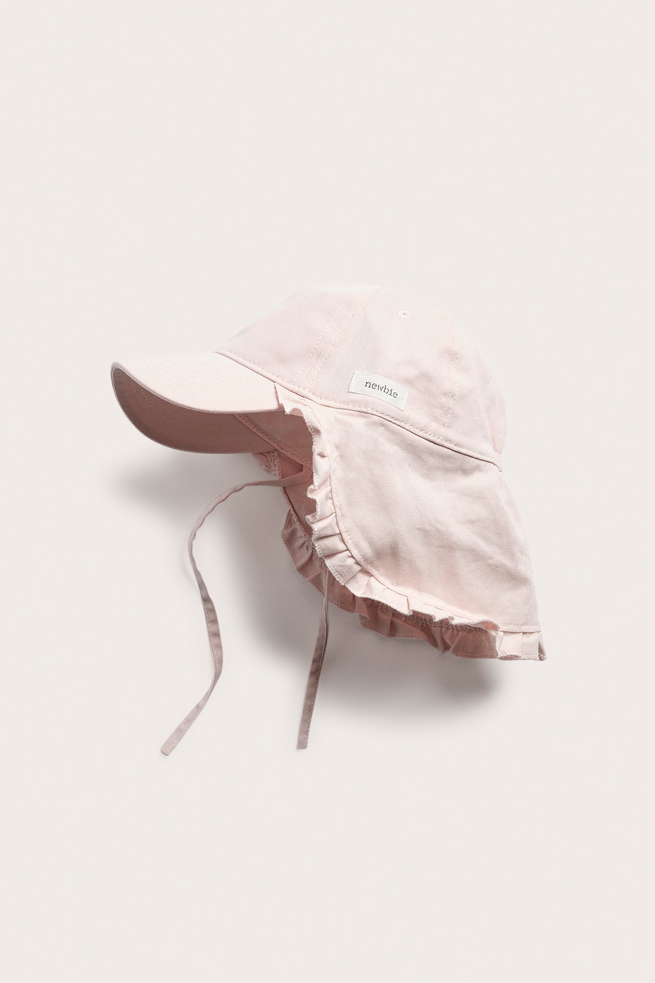 Side view of a solid pink baby cap with a wide ruffled sun shield and chin tie straps.