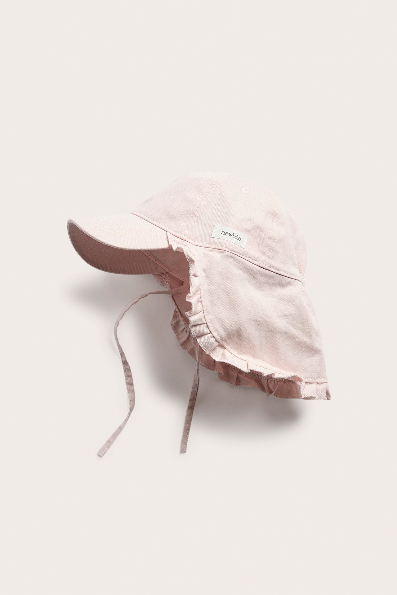 Side view of a solid pink baby cap with a wide ruffled sun shield and chin tie straps.