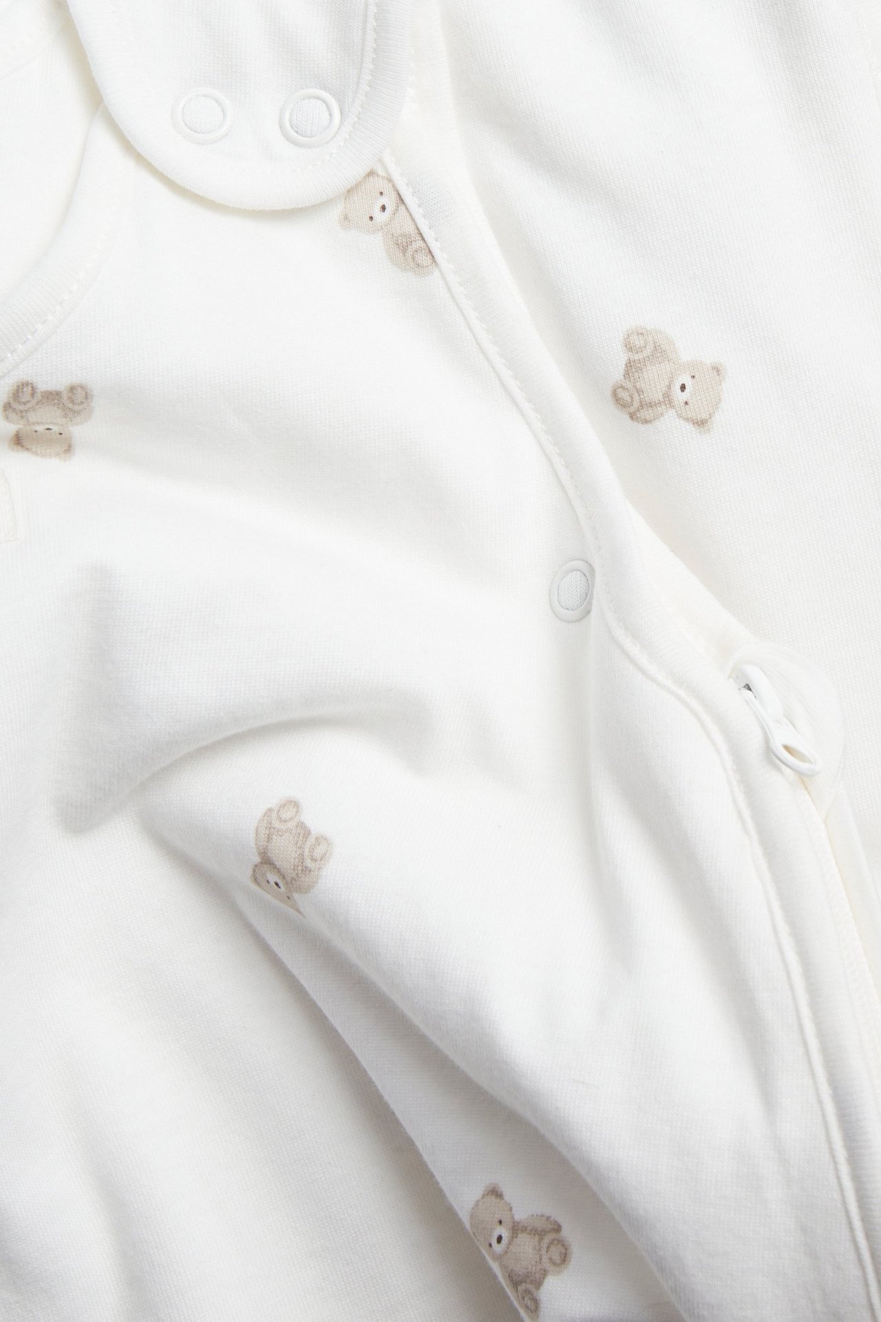 Nahaufnahme eines cremeweißen Babyschlafsacks mit hellbraunem Bärenmuster, Druckknöpfen und Zwei-Wege-Reißverschluss.