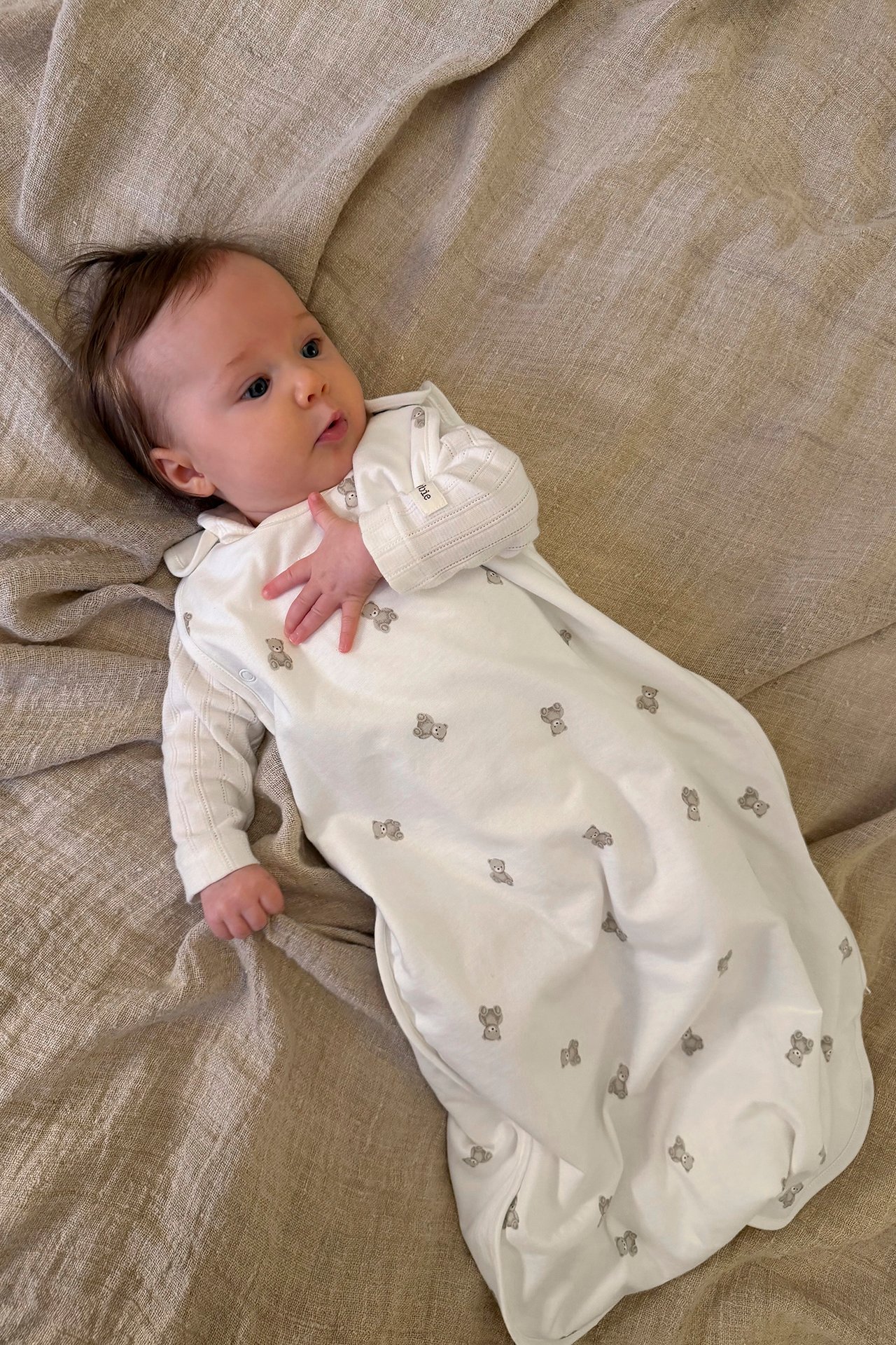 Overhead view of a baby in an off-white sleeping bag with bear print over a striped long-sleeve top.