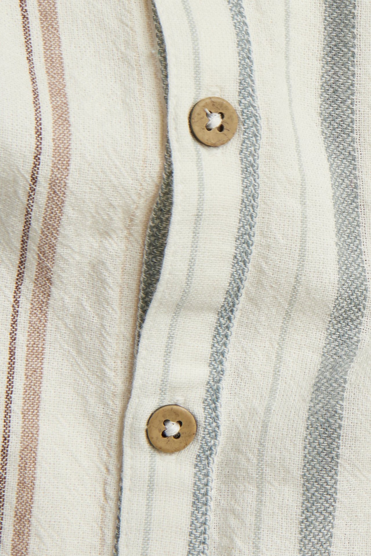 Nahaufnahme eines off-white gestreiften gewebten Baumwoll-Rompers mit sichtbaren Holzknöpfen an der vorderen Knopfleiste.