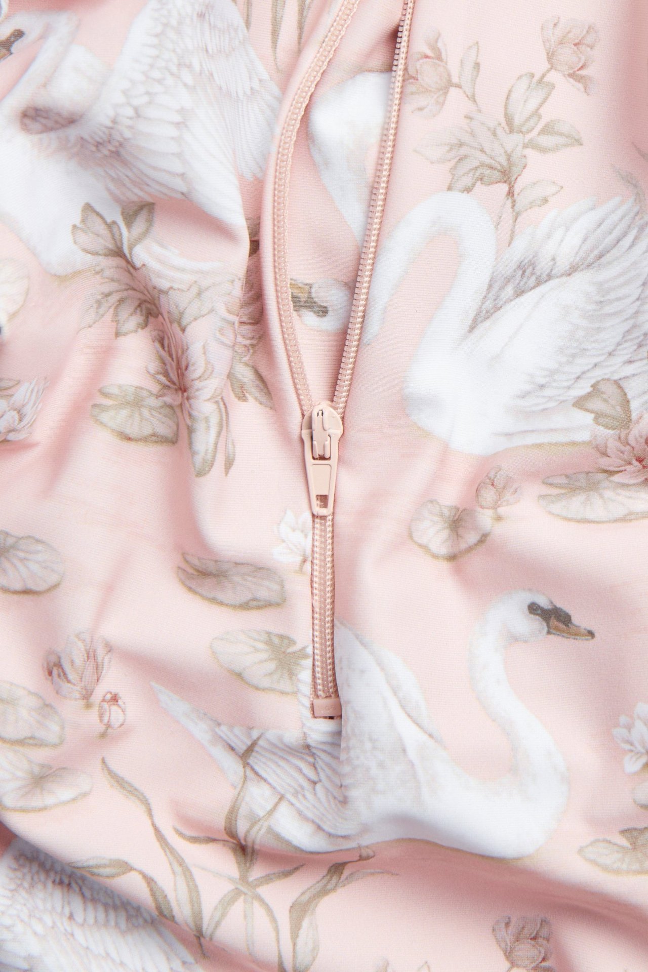 Nahaufnahme eines rosa UV-Overalls mit weißem Schwan- und Blumenmuster, mit Reißverschluss.