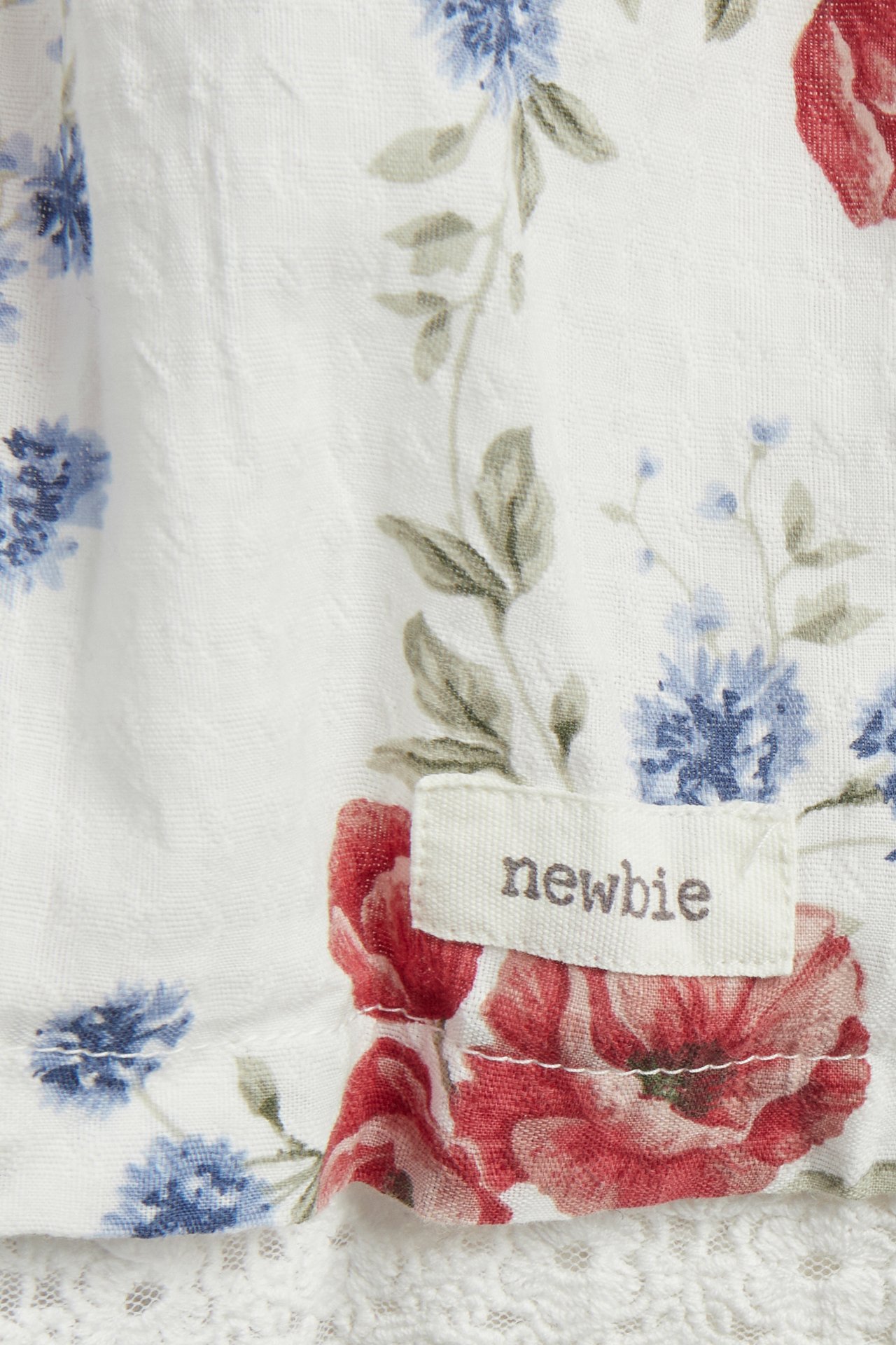 Nahaufnahme eines cremefarbenen gewebten Blumenkleides mit roten und blauen Blumen, Spitzenkante und Newbie-Etikett.
