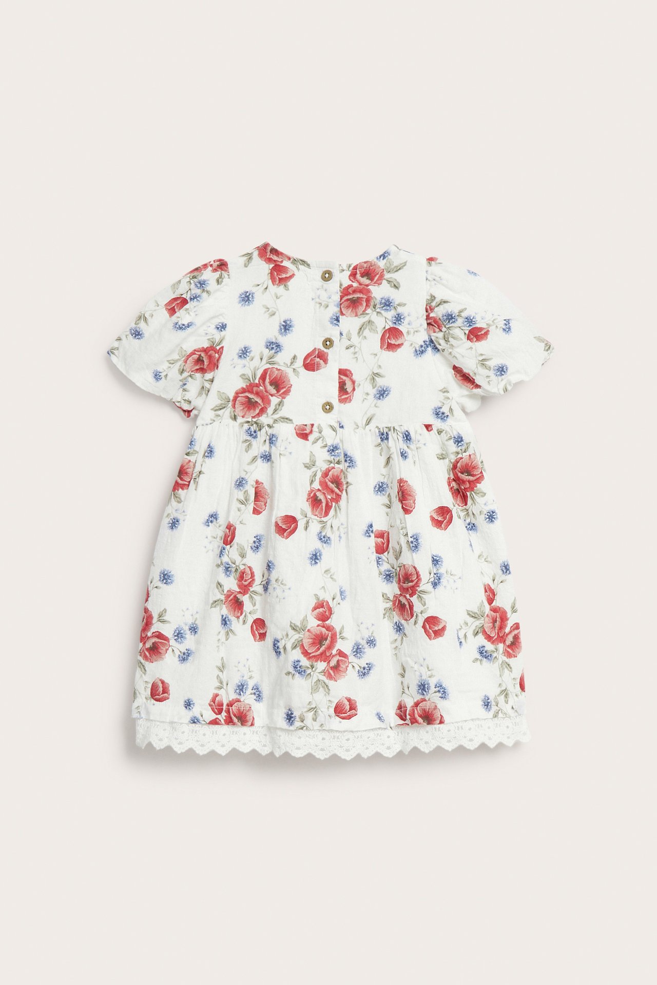Rückenansicht eines cremeweißen Kinderkleides mit Blumenmuster, Puffärmeln, Spitzenbündchen und Knöpfen hinten.
