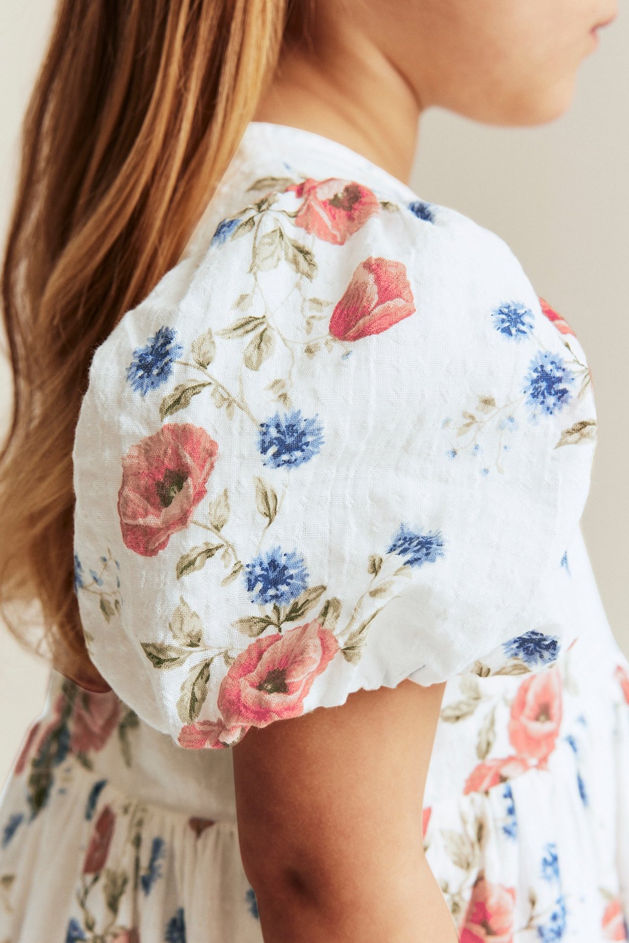 Side-back view of a kid wearing an off-white floral dress with short, puffy sleeves.