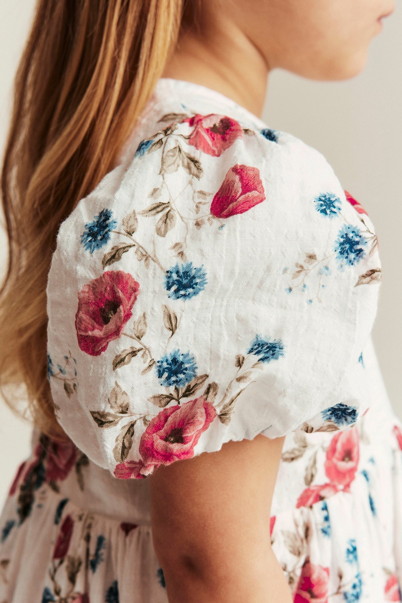 Seitenansicht eines Kindes in einem cremefarbenen Blumenkleid mit rosa und blauen Blumen und Ballonärmeln.